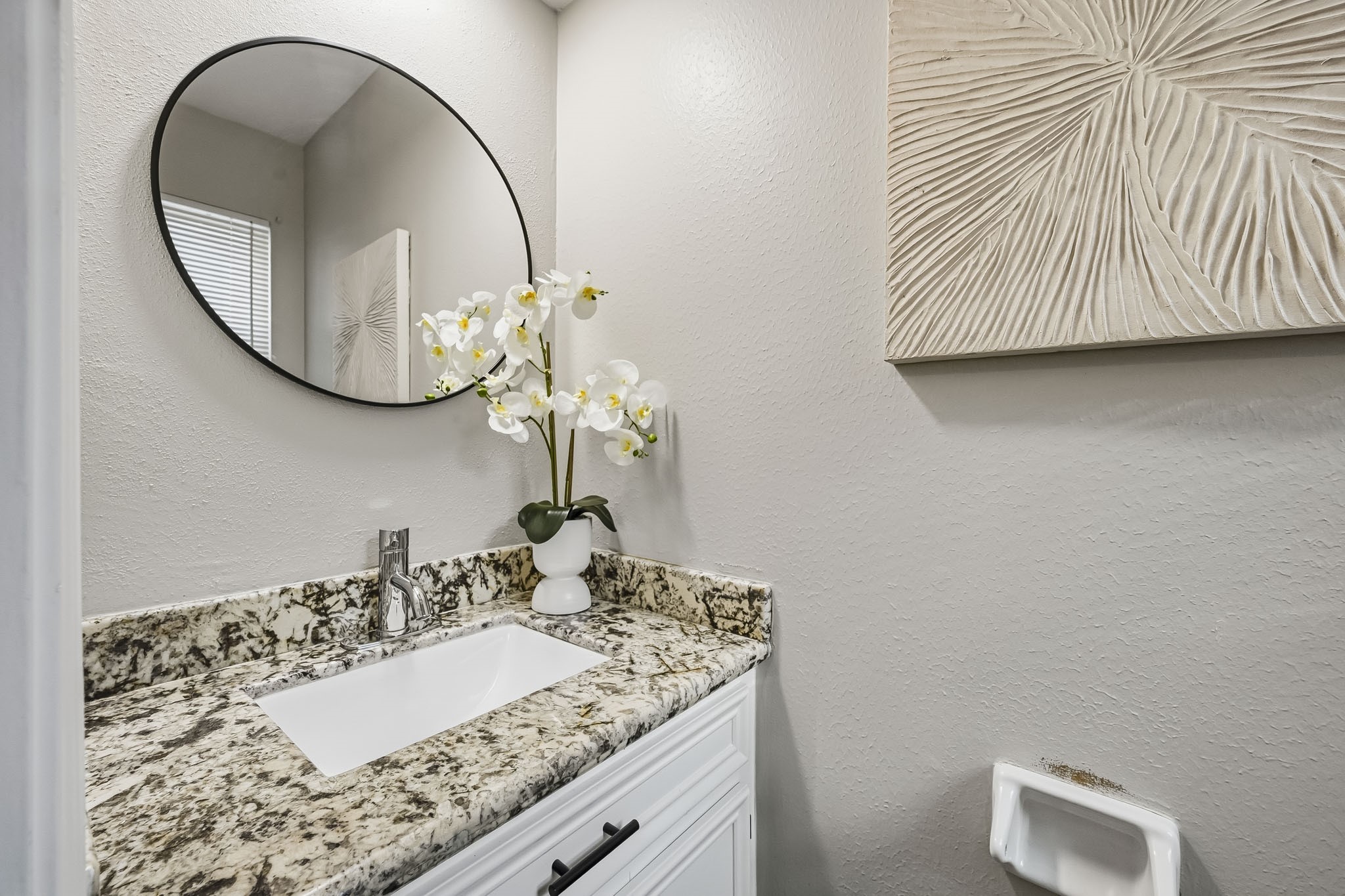 Chic and modern bathroom featuring a sleek granite countertop, elegant oval mirror, and stylish contemporary decor, offering a serene and sophisticated ambiance.