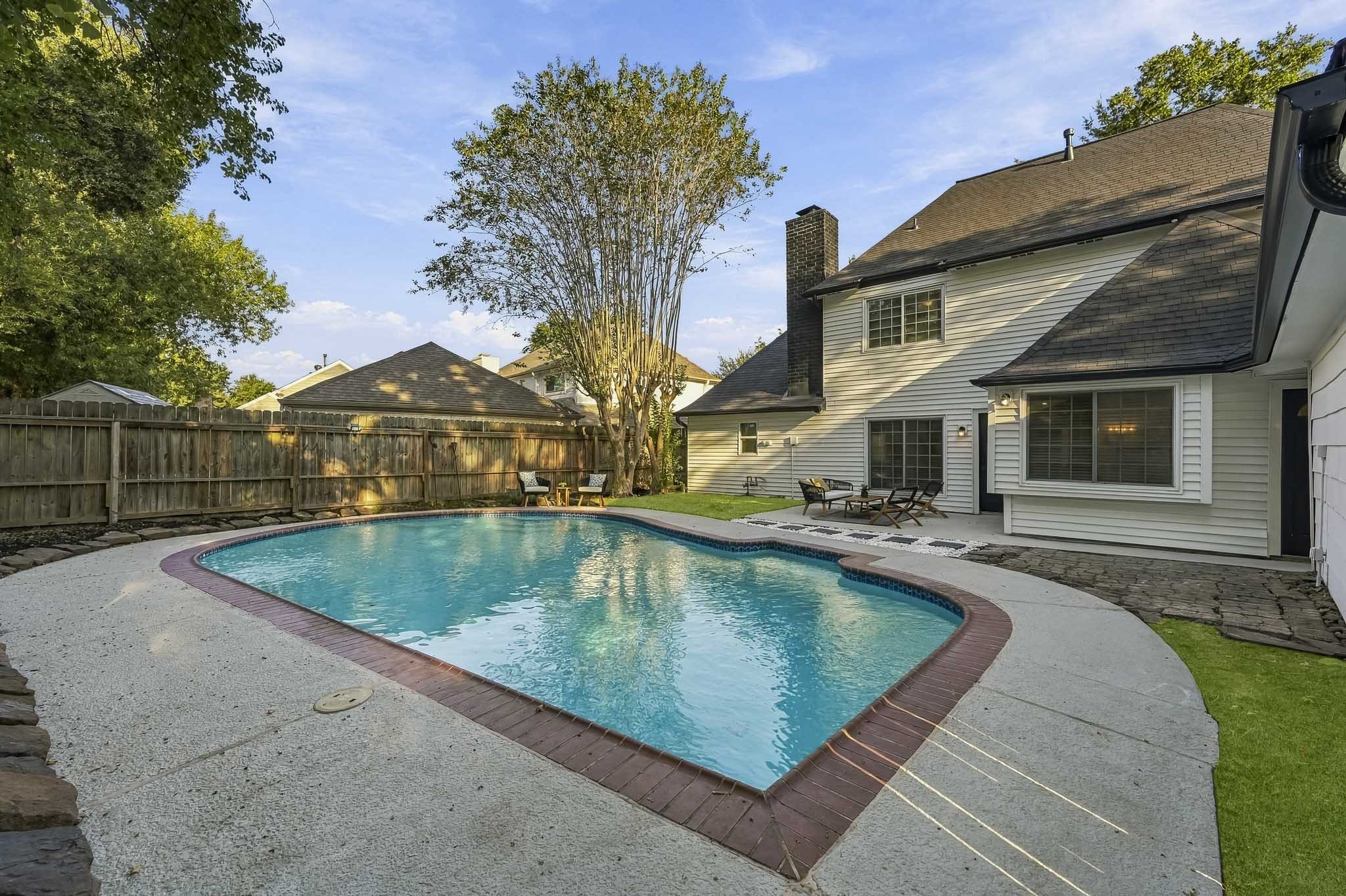 Charming backyard oasis with a sparkling in-ground pool, surrounded by lush greenery and a spacious patio perfect for outdoor relaxation and entertaining.