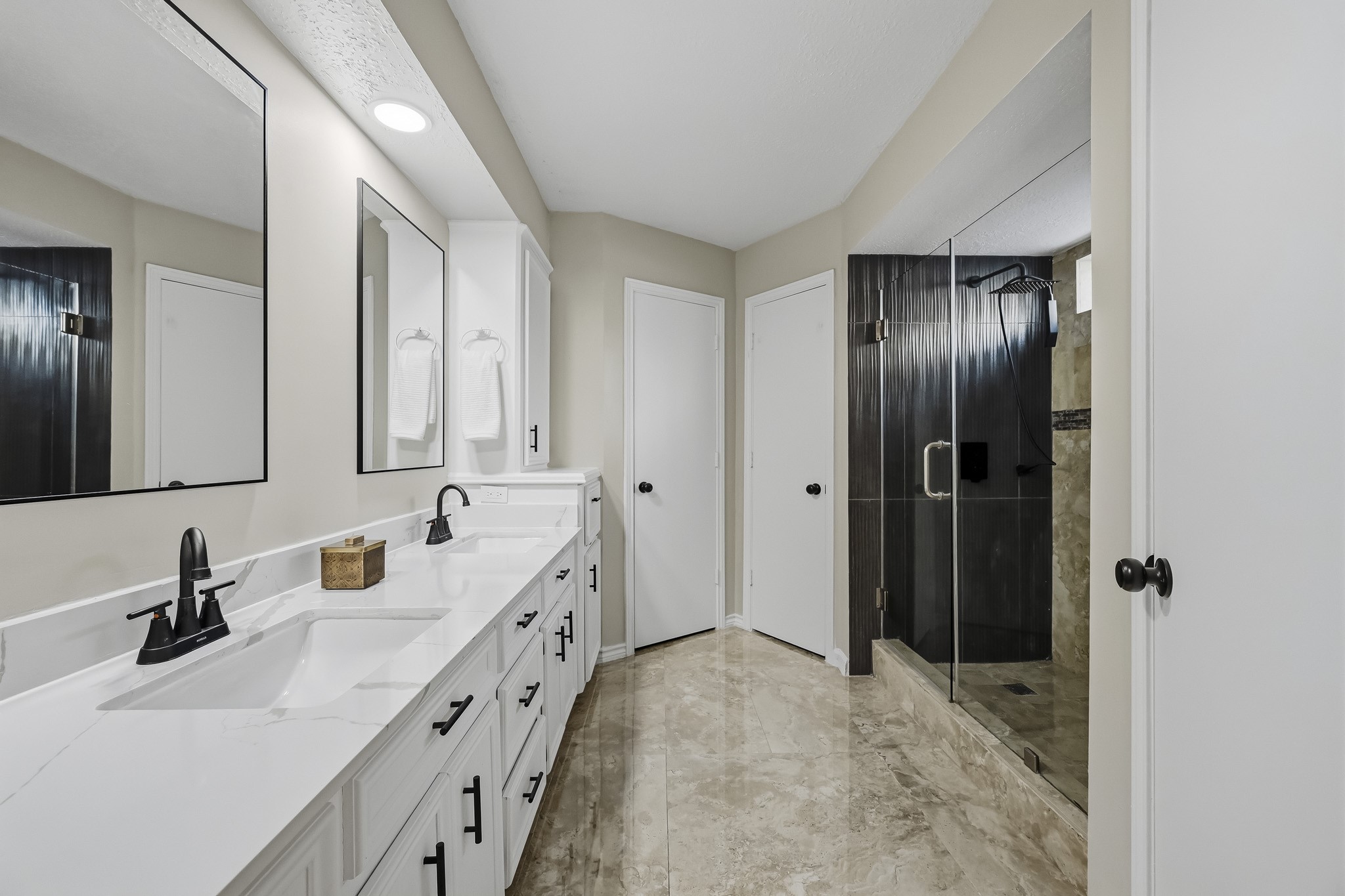 Elegant bathroom featuring a spacious double vanity with sleek black fixtures, complemented by a luxurious glass-enclosed shower and ample storage.