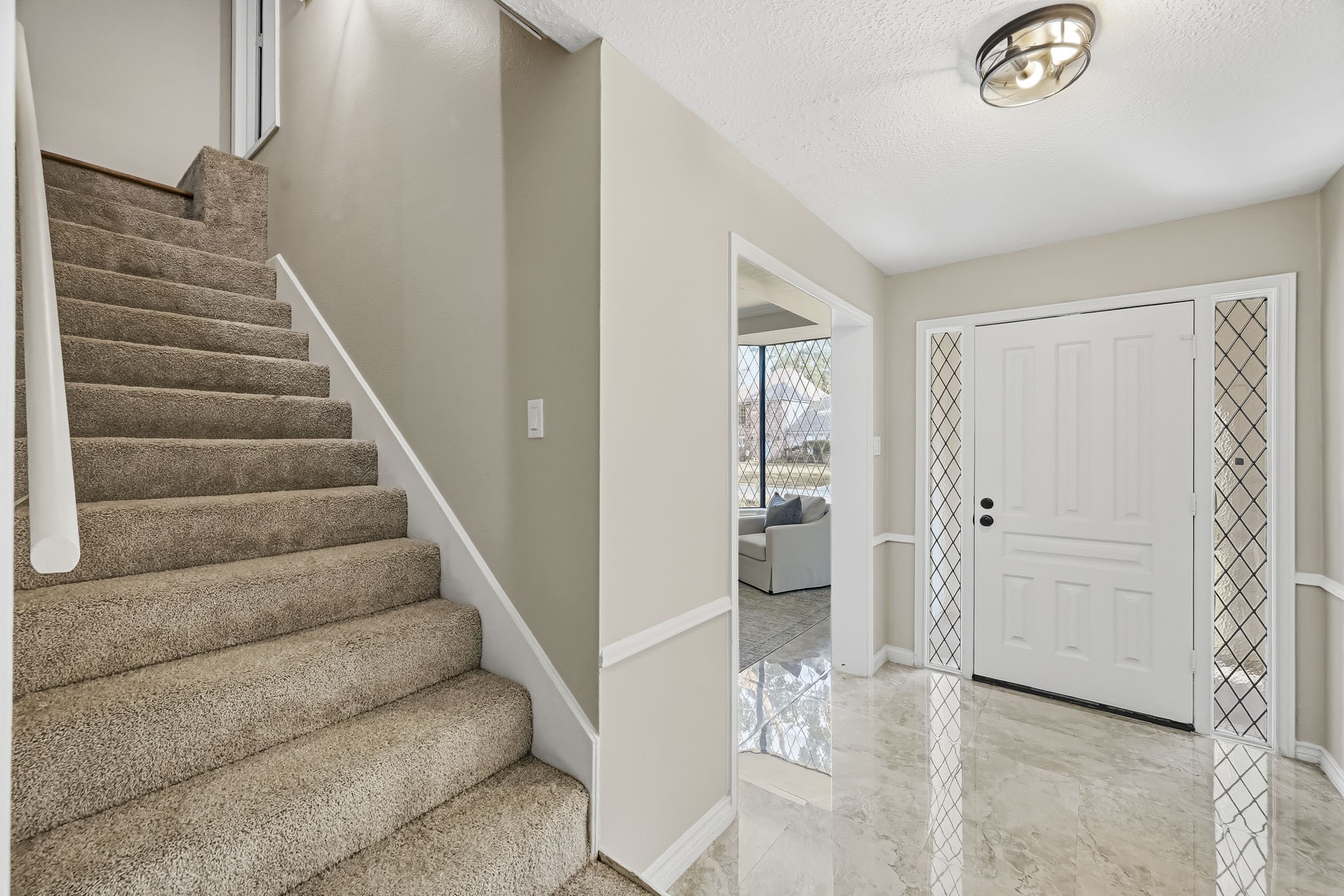 Inviting entryway featuring elegant marble flooring, a classic white door with decorative side panels, and plush carpeted stairs leading to the second floor.