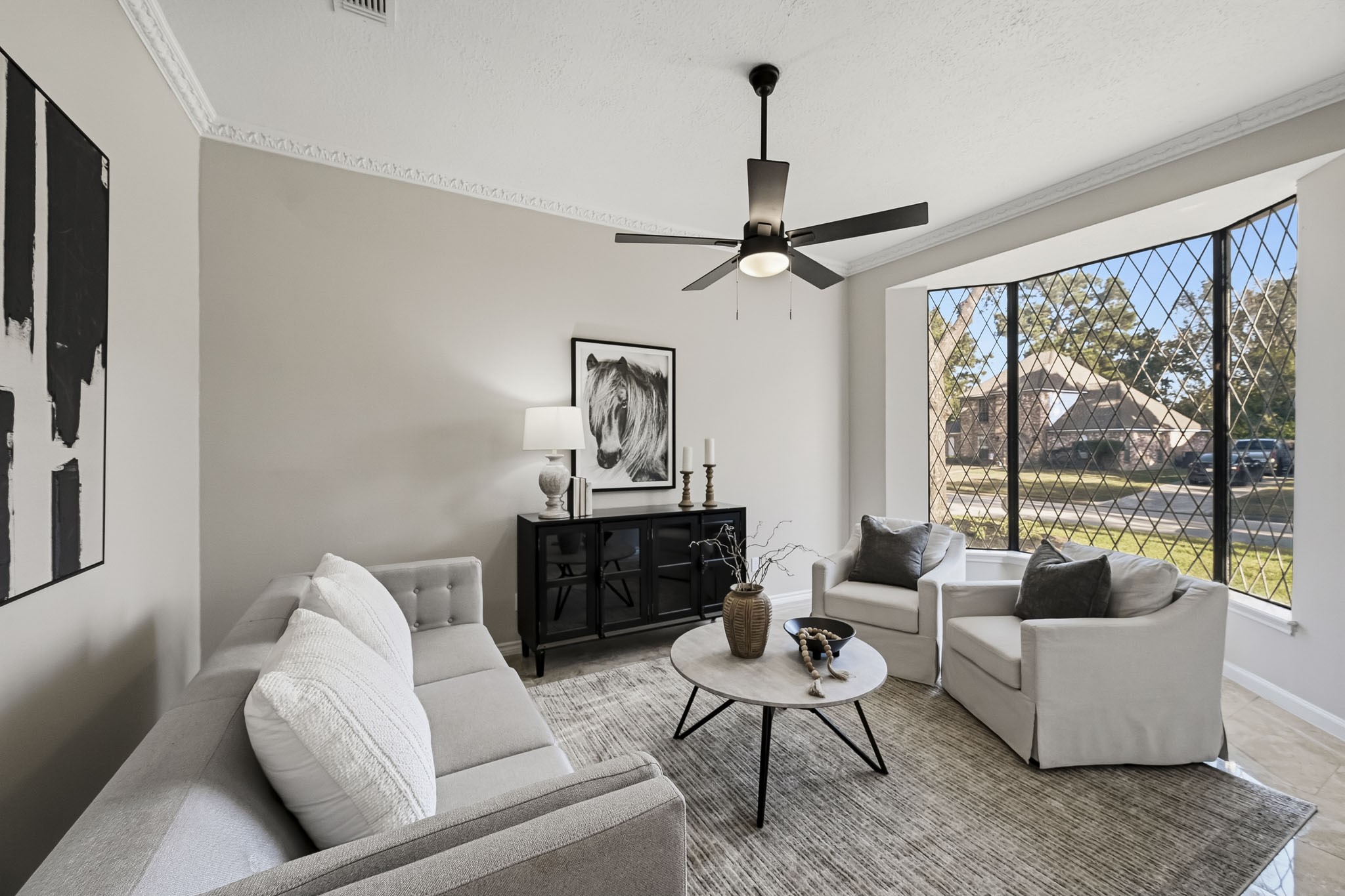 Charming living room with a modern ceiling fan, large diamond-patterned windows allowing natural light, and stylish neutral furnishings creating an inviting atmosphere.