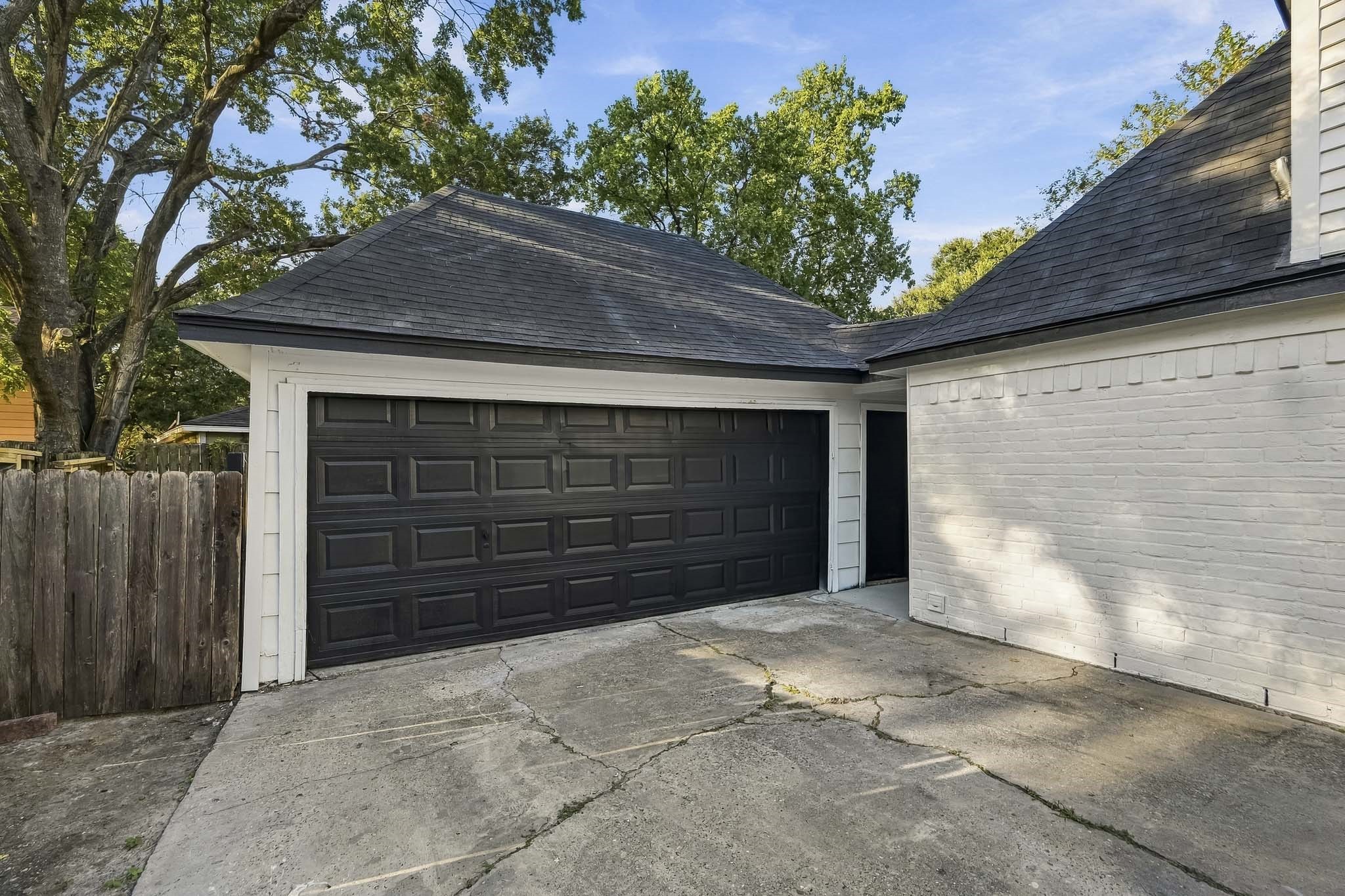 Spacious two-car garage with a sleek black door, set against a charming white brick exterior, offering easy access and ample driveway space.