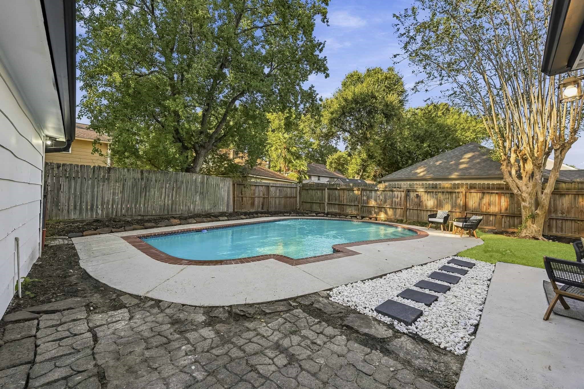 Enjoy a refreshing retreat in this spacious backyard featuring a sparkling pool, surrounded by a privacy fence and lush greenery.