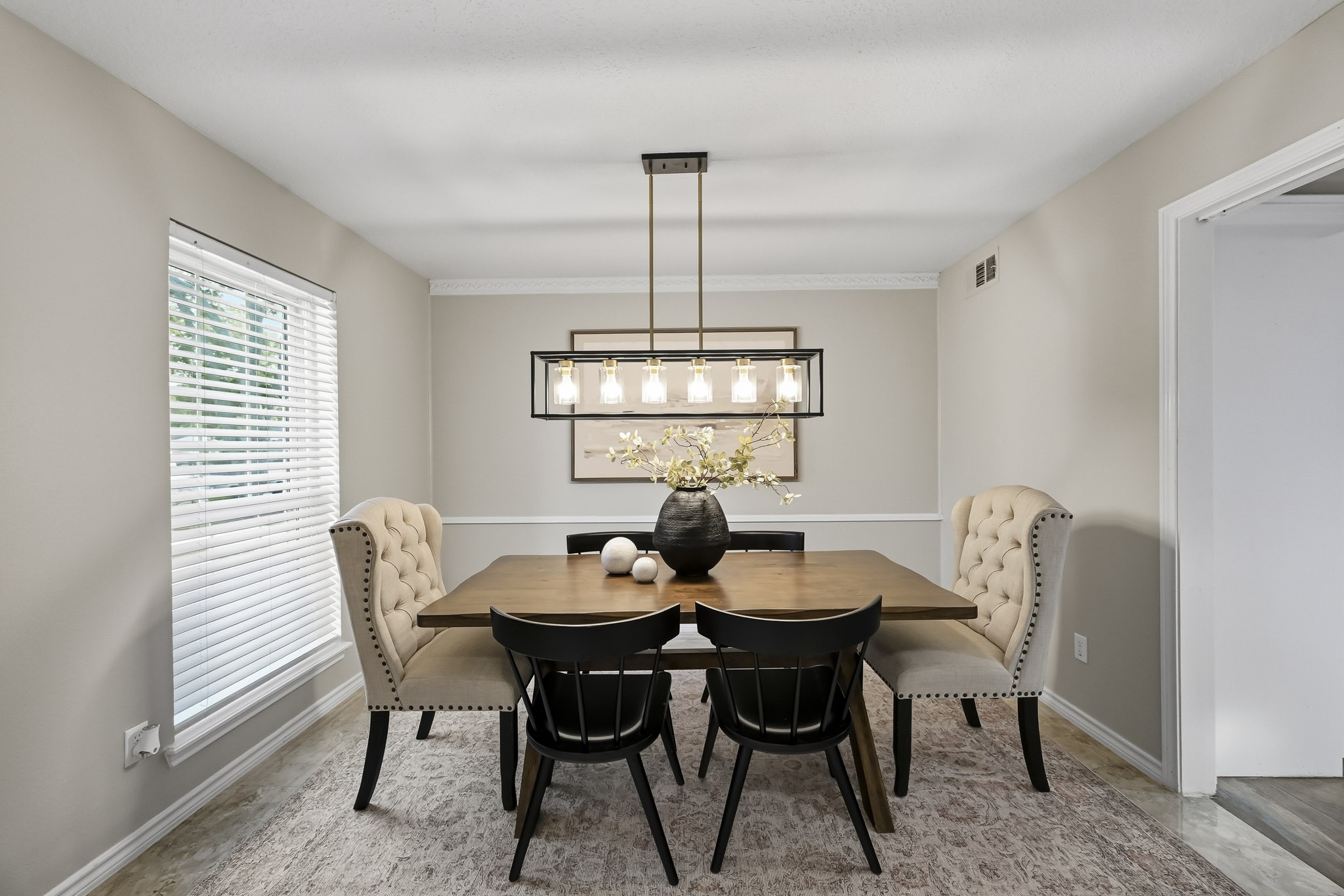 Elegant dining room featuring a stylish chandelier, a wooden table with seating for six, and plush upholstered chairs, accented by soft natural light from a large window.