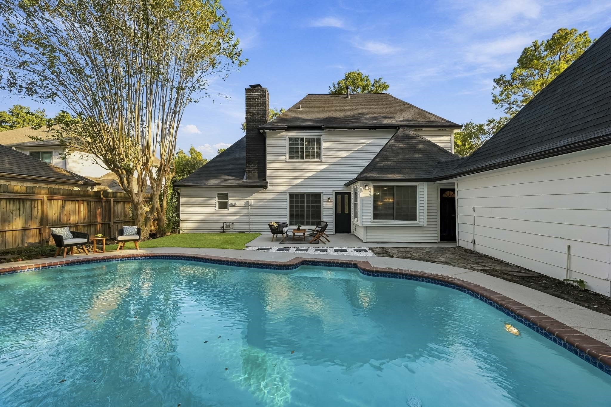 Charming two-story home with a spacious backyard featuring a sparkling pool, surrounded by mature trees and a cozy patio area perfect for relaxation and entertaining.