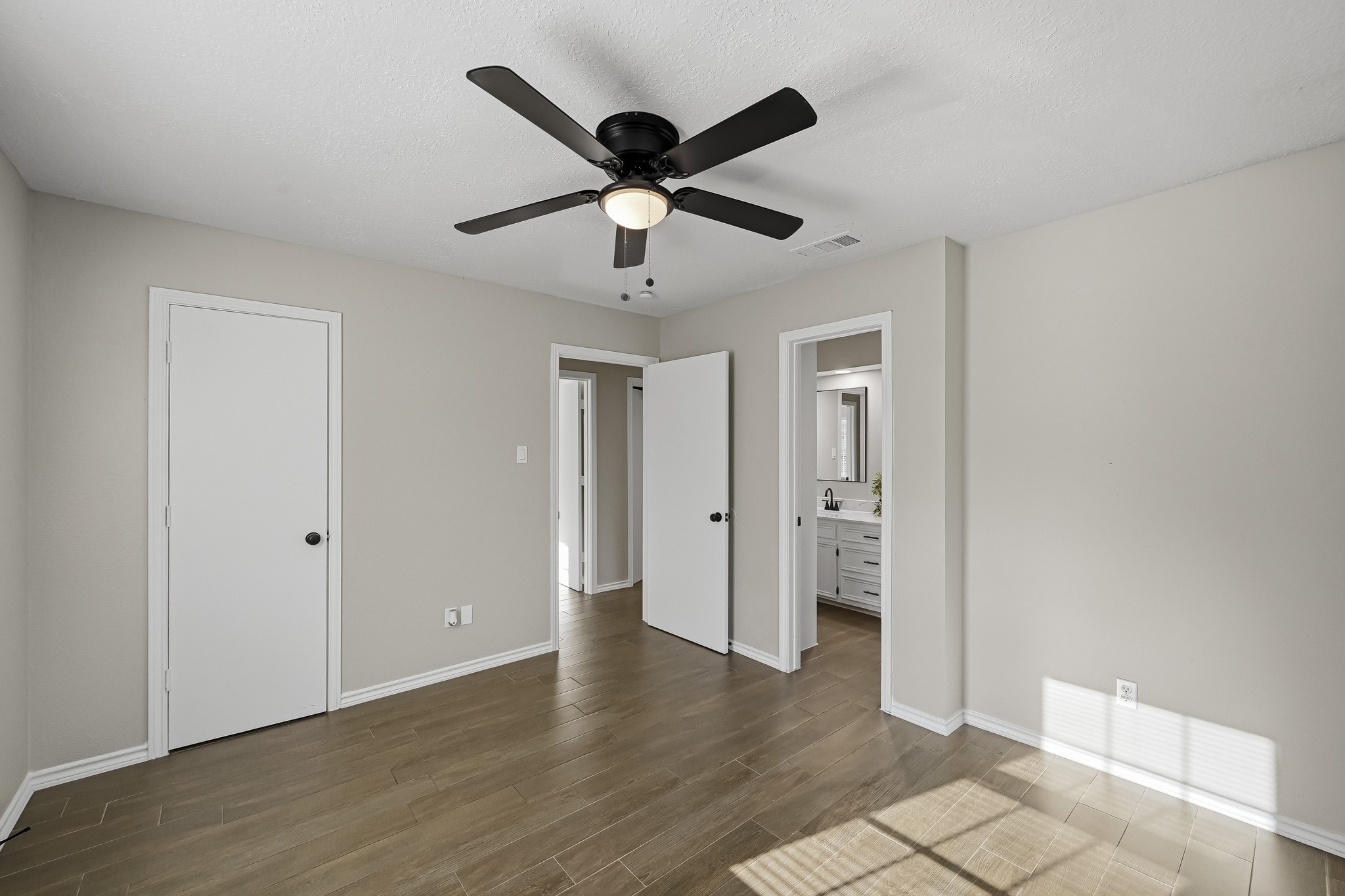 Bright and airy room featuring sleek wood flooring, a modern ceiling fan, and direct access to a stylish bathroom.