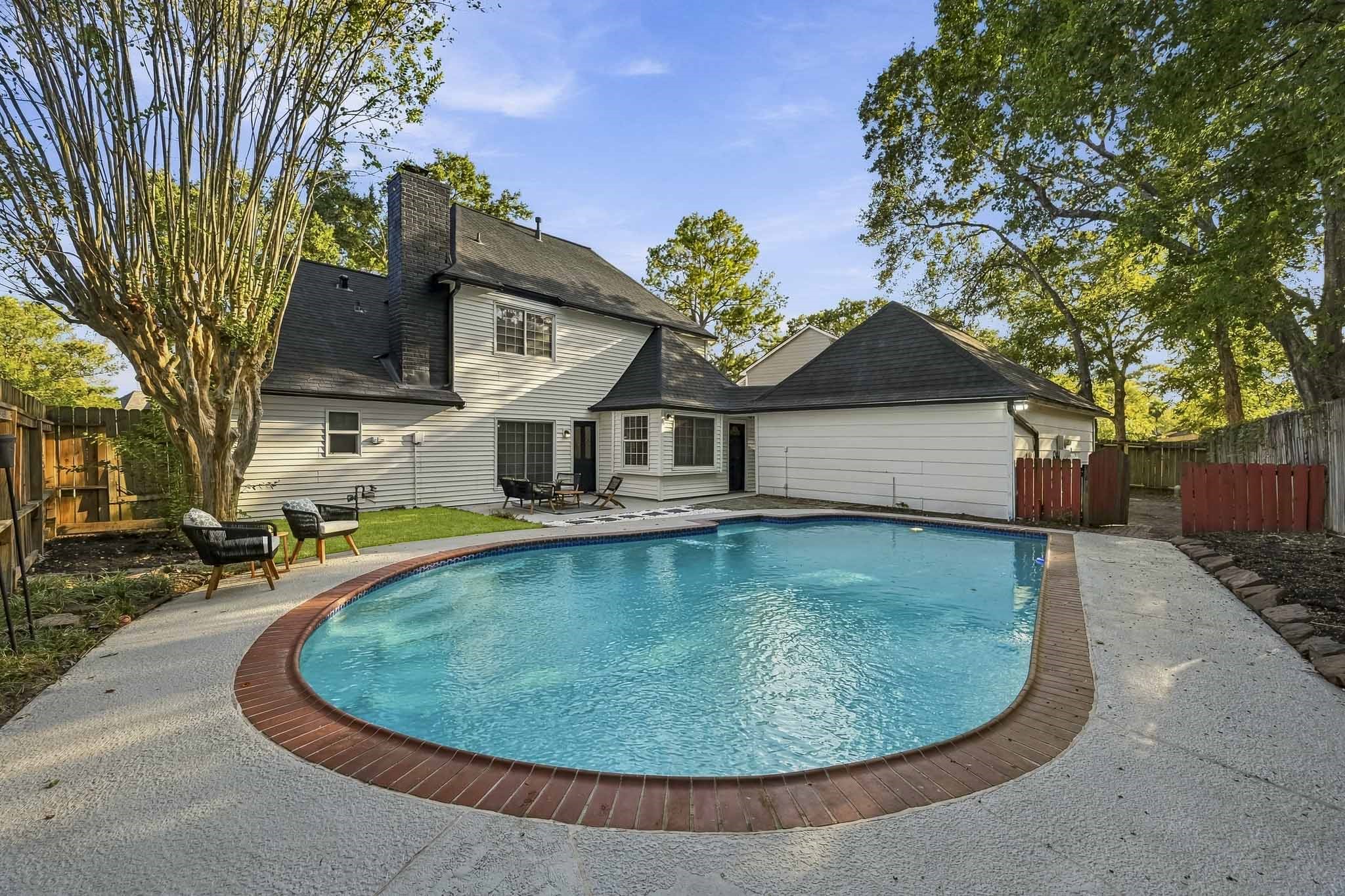 Inviting backyard oasis with a sparkling pool, surrounded by mature trees and ample patio space for relaxation and entertainment.