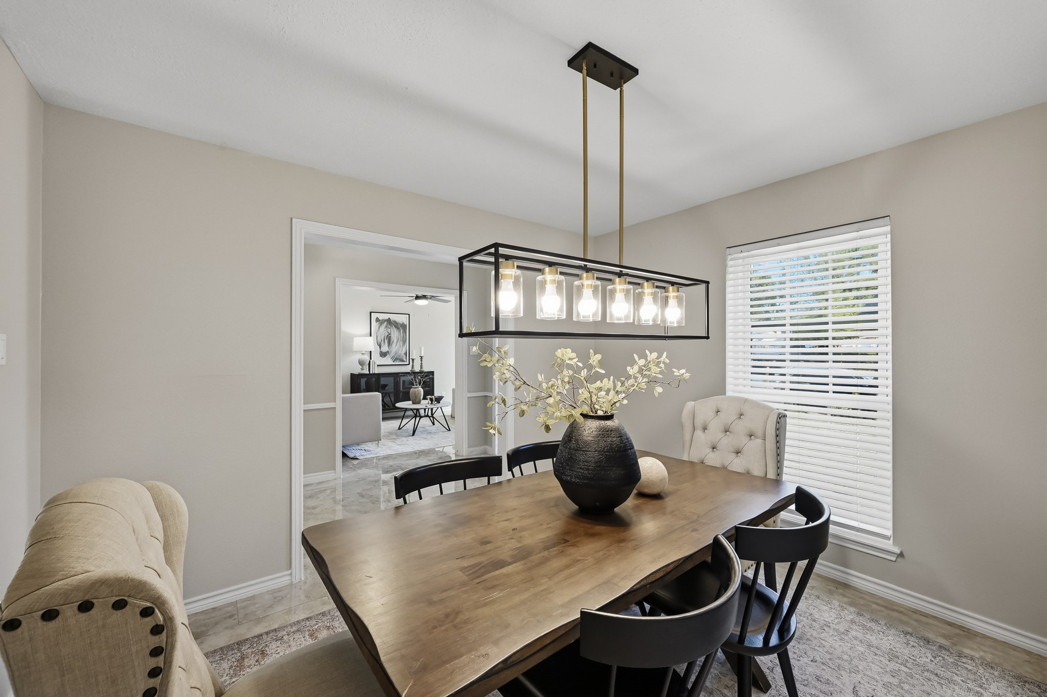 Elegant dining room featuring a wooden table, modern chandelier, and natural light from a large window, creating a cozy and inviting atmosphere.