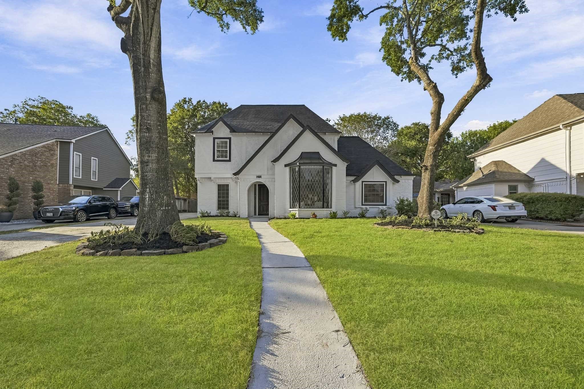 Charming two-story home with a classic black and white exterior, nestled between mature trees and featuring a welcoming arched entrance.