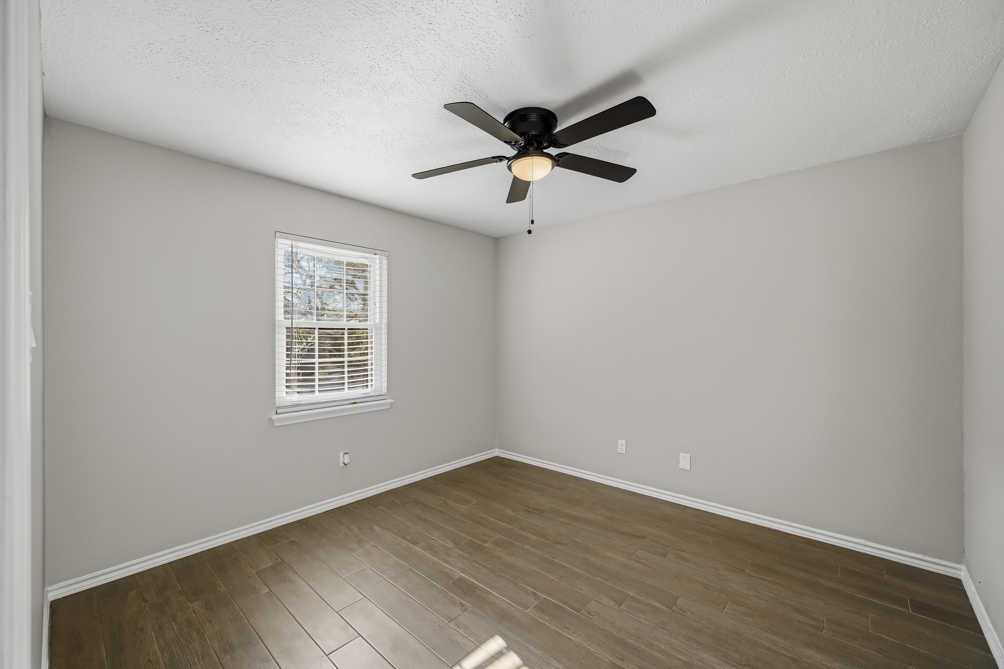 Bright and inviting bedroom featuring sleek wooden floors, a modern ceiling fan, and ample natural light through a large window.