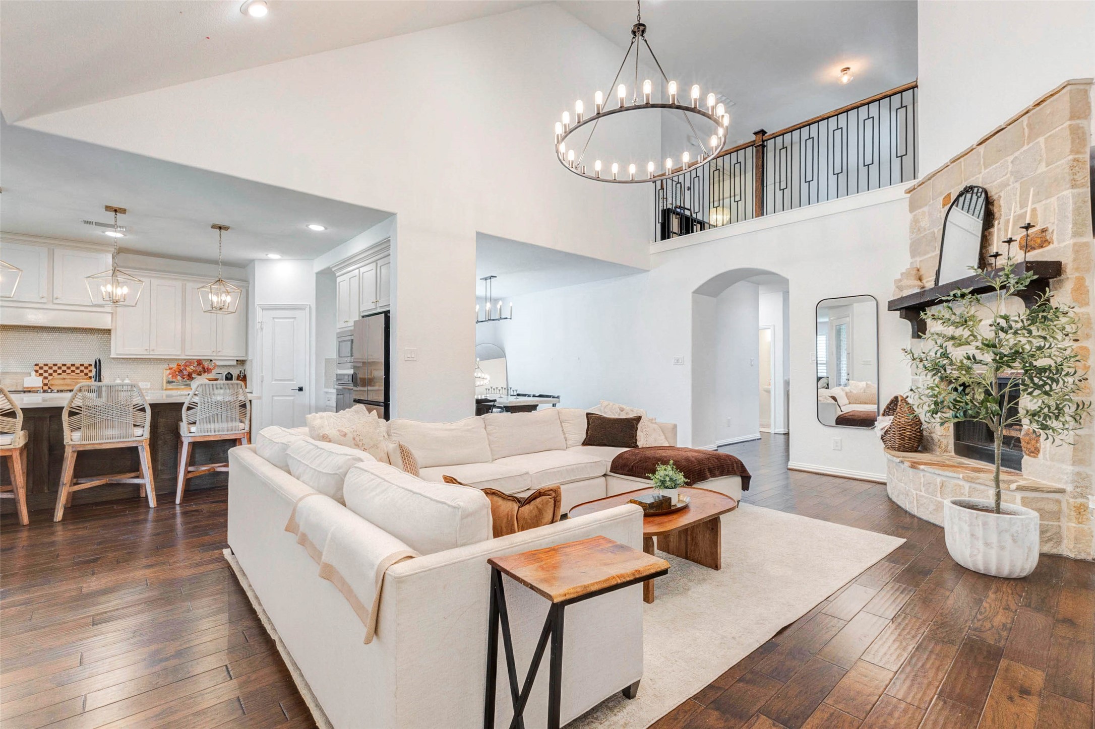 An impressive open-concept layout connects the living room effortlessly to the kitchen and dining areas, creating a perfect space for gathering. The elevated ceilings and second-story overlook add depth and architectural appeal. Rich wood flooring ties the space together, while the fireplace serves as a cozy focal point. This layout offers flexibility and a natural flow ideal for modern living and entertaining.