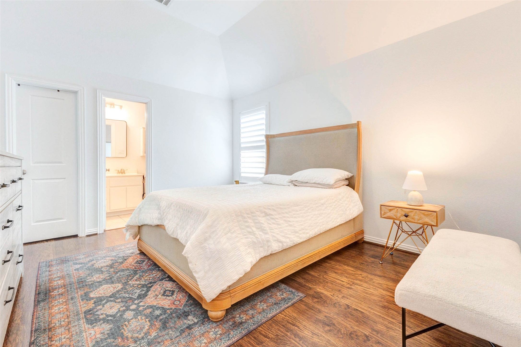 This spacious bedroom offers a serene and airy feel with its high ceilings and soft neutral finishes. Rich wood flooring adds warmth, while the open layout provides flexibility for furniture placement. Natural light streams in, enhancing the peaceful ambiance. With convenient access to a nearby bathroom, this room offers comfort and convenience in a well-designed space