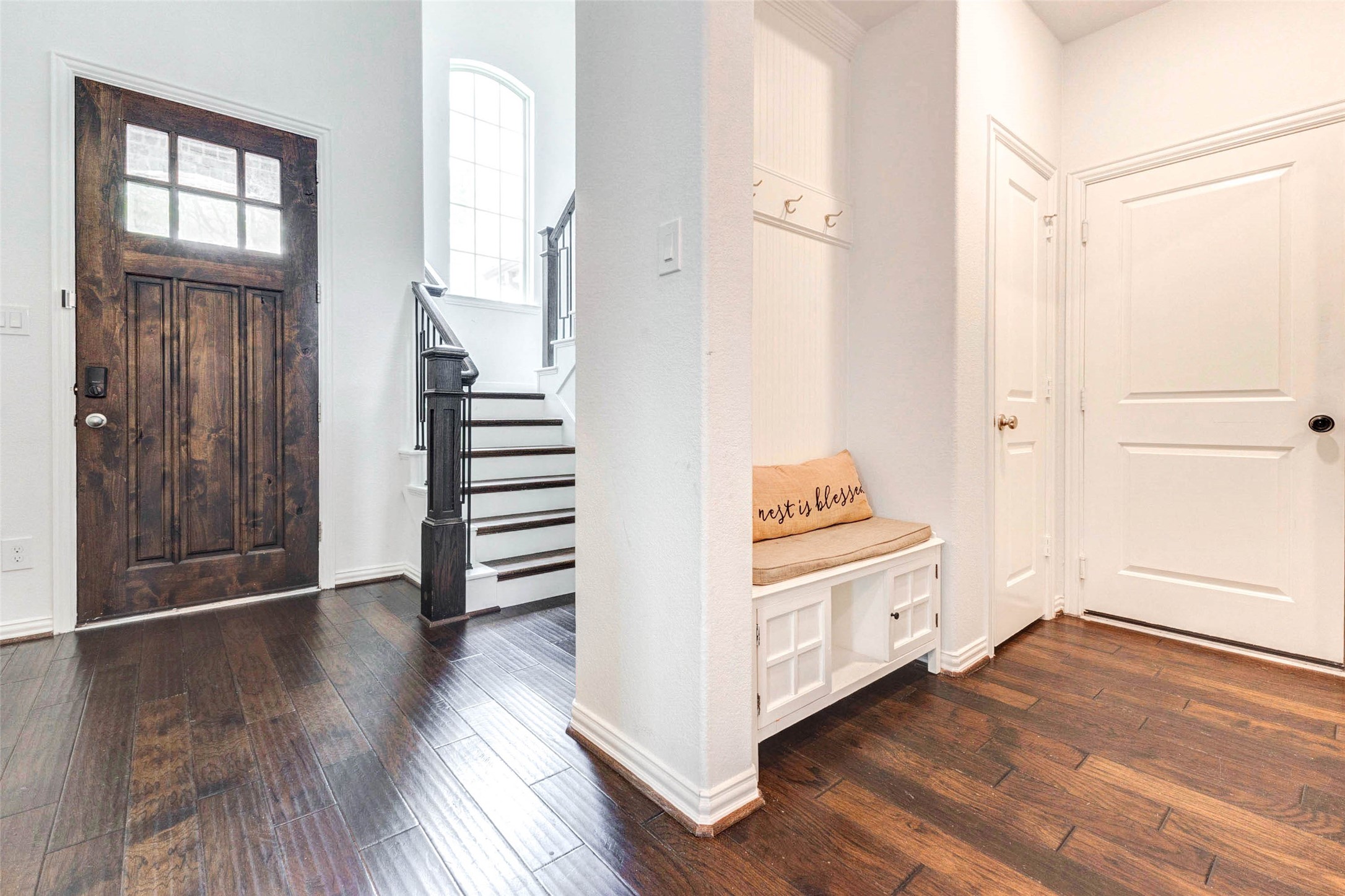 Step inside to a bright and inviting entryway where rich wood flooring and a stunning front door set a warm, upscale tone. Natural light pours in through the tall window, highlighting the clean lines and open feel. A built-in bench offers both charm and functionality, while the staircase with dark wood accents adds architectural interest. This thoughtfully designed space creates a welcoming transition into the heart of the home.