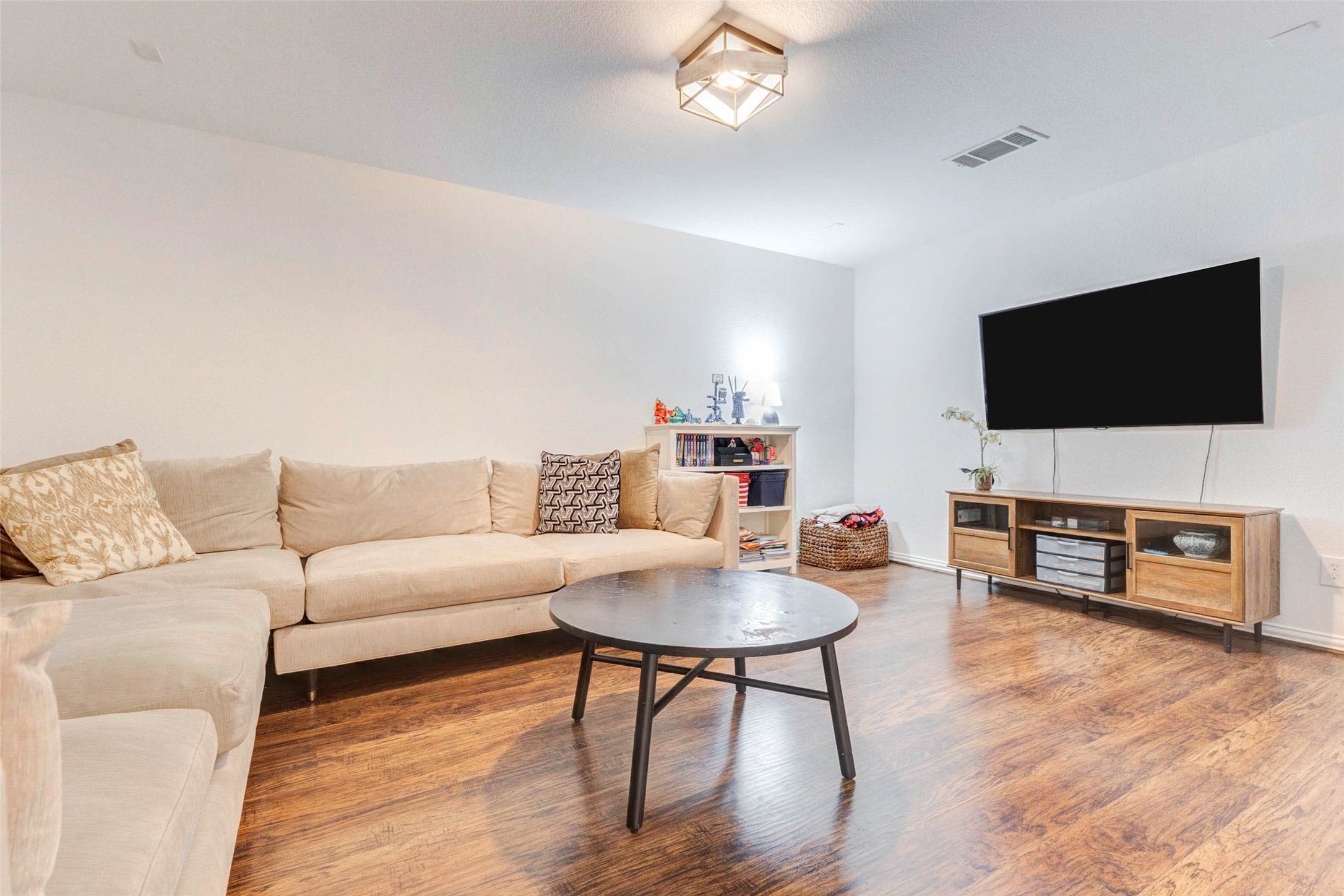 This cozy secondary living space works well as a media room, game room, or lounge. The neutral tones and warm wood flooring create an inviting atmosphere, while the open layout allows for flexible furniture arrangements. A mounted TV and additional storage make this space both practical and comfortable, offering a private retreat ideal for entertainment, gaming, or unwinding at the end of the day.
