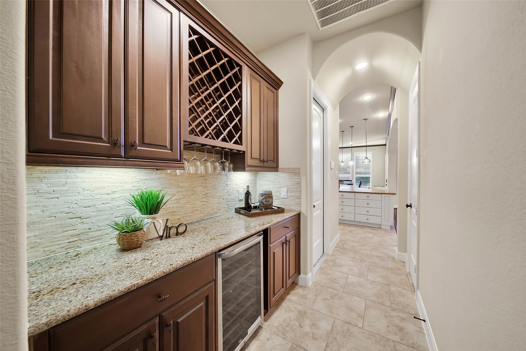 Perfect for entertaining, the butlers pantry features upper cabinets to store barware, a built-in wine rack, and generous storage for additional china and stemware. Granite counters with travertime backsplash anchors the space, complemented by abundant lower storage and a wine chiller.