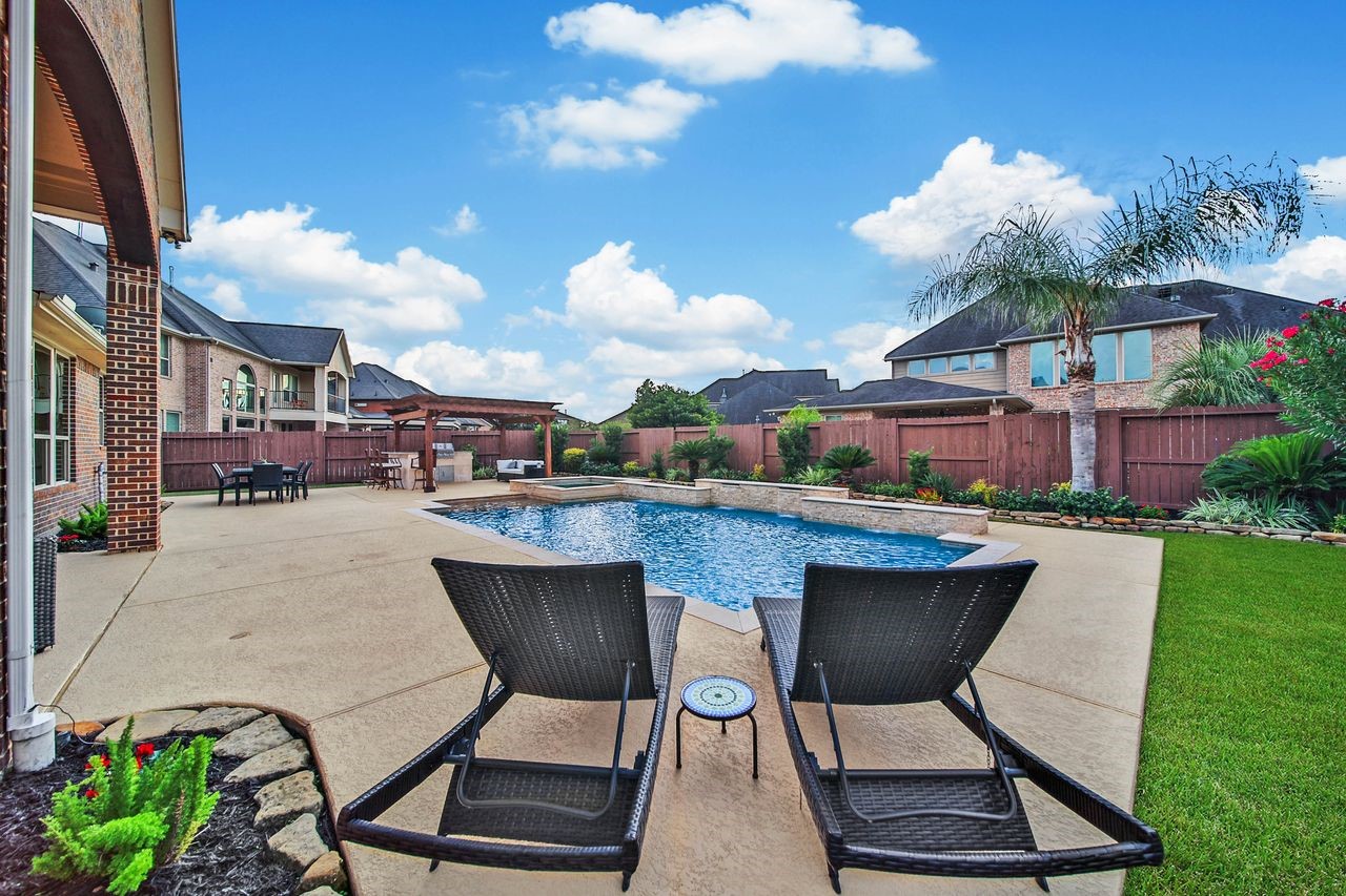 Lush landscaping frames the backyard with natural beauty, creating a serene and picturesque setting to enjoy throughout the year. Three built-in umbrella holes around the pool decking provide convenient options for adding shade, keeping you cool and comfortable while enjoying the backyard oasis.