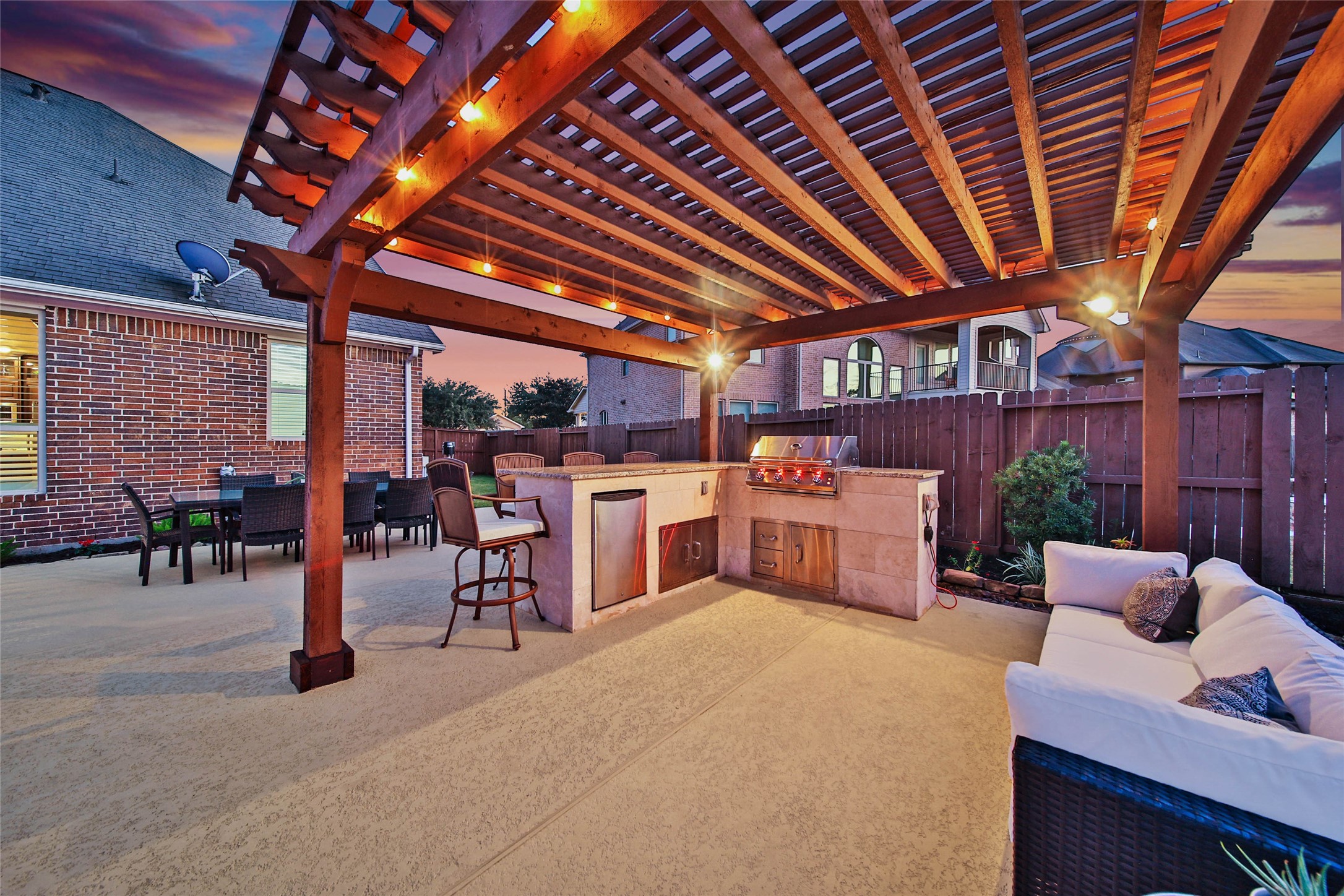 The custom pergola creates a second covered gathering space, complete with an outdoor kitchen featuring a 2026 Kokomo grill and mini refrigerator. This inviting dining and conversation area offers yet another fabulous spot to dine al fresco plus entertain family and friends!  Built-in interior lights on the Kokomo illuminate the cooking surface so you can see your food clearly while grilling at night!