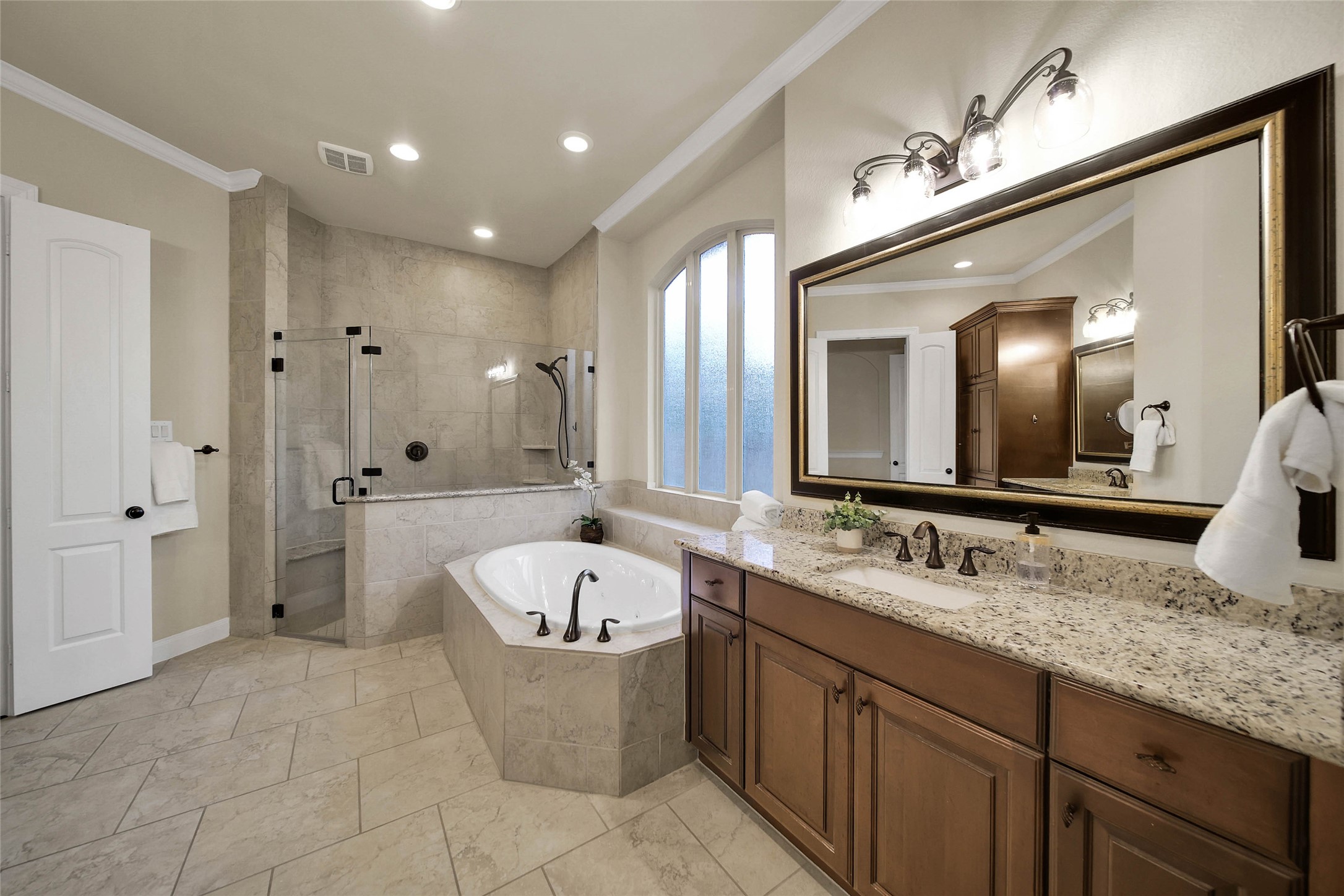 The spacious primary bath features a relaxing jetted tub, a frameless glass shower, and plenty of room for two to comfortably get ready for the day.