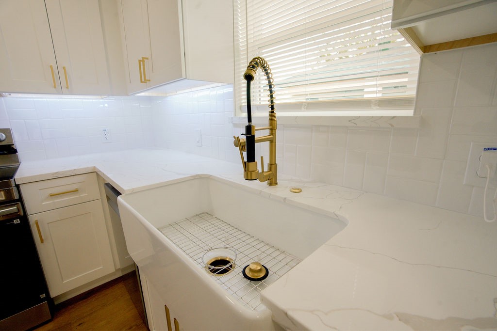 Elegant kitchen featuring a farmhouse sink with a stylish brass faucet, complemented by sleek white cabinetry and modern quartz countertops.