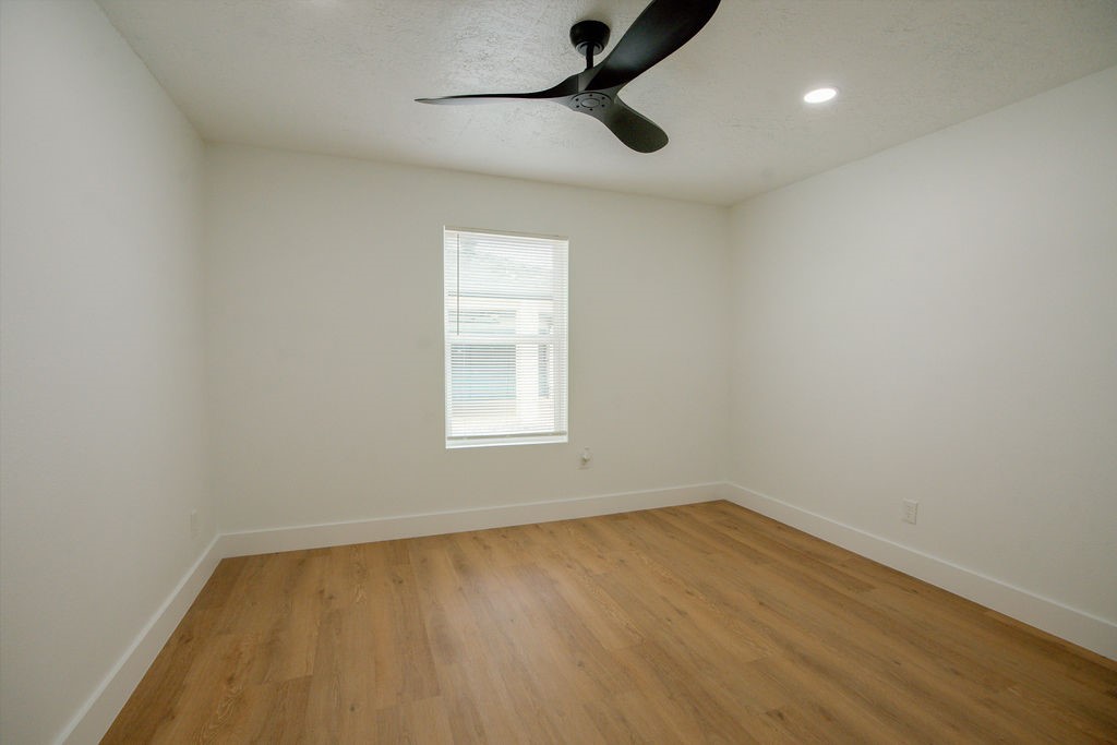 Bright and spacious room featuring sleek hardwood style flooring, a modern ceiling fan, and a large window inviting natural light.