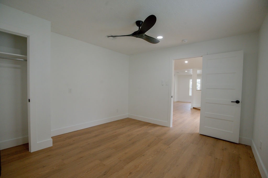 Spacious bedroom featuring sleek hardwood style floors, a modern ceiling fan, and ample natural light from the adjoining room.
