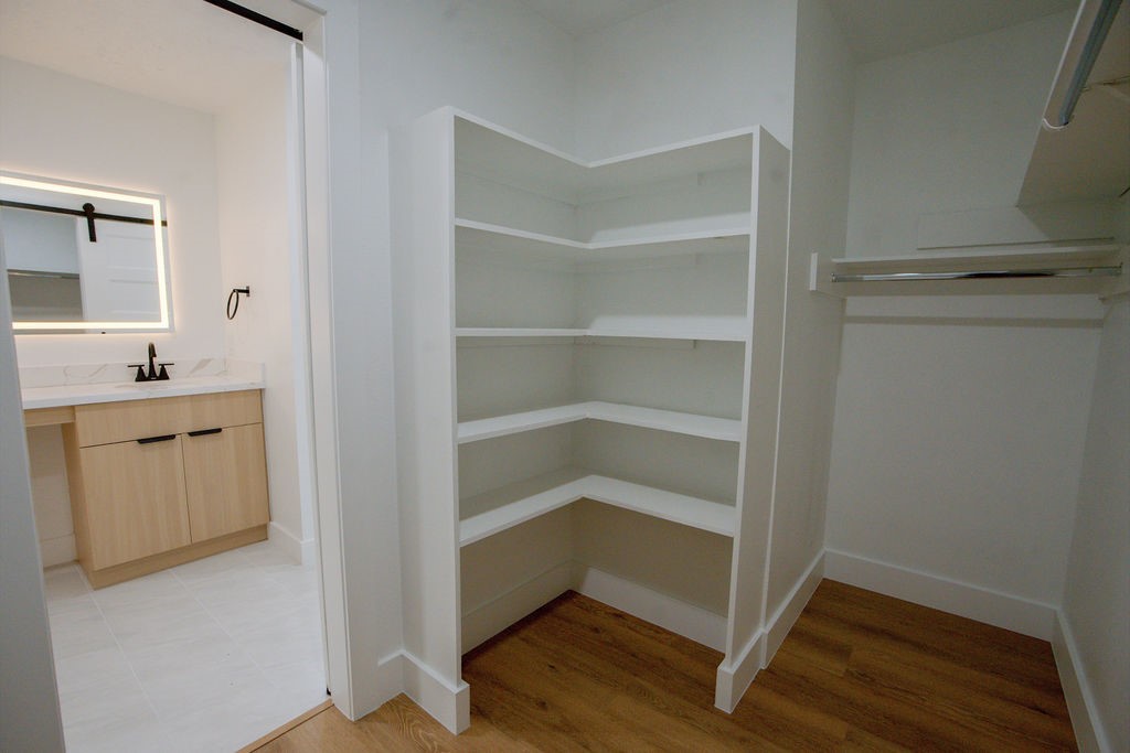 Spacious walk-in closet with built-in shelving, adjacent to a modern bathroom featuring a stylish vanity and mirror.