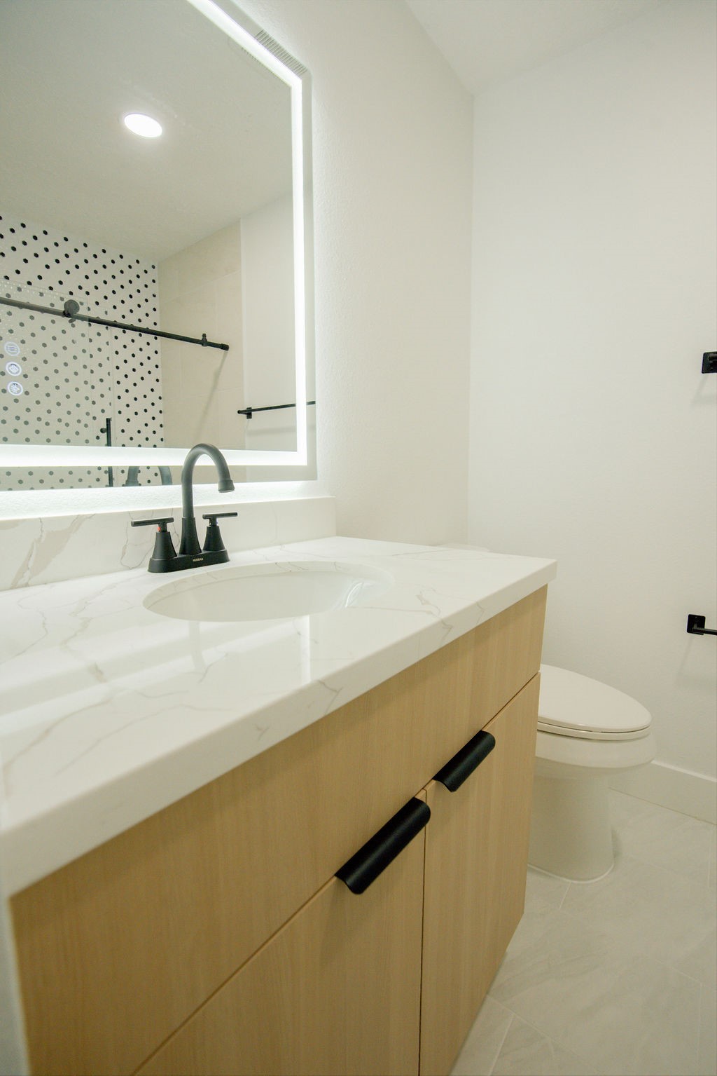 Modern bathroom featuring a sleek vanity with a quartz countertop, stylish black fixtures, and a backlit mirror.