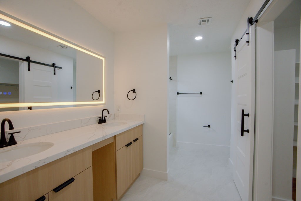 Sleek modern bathroom featuring a double vanity with elegant black fixtures, illuminated mirror, and sliding barn doors.