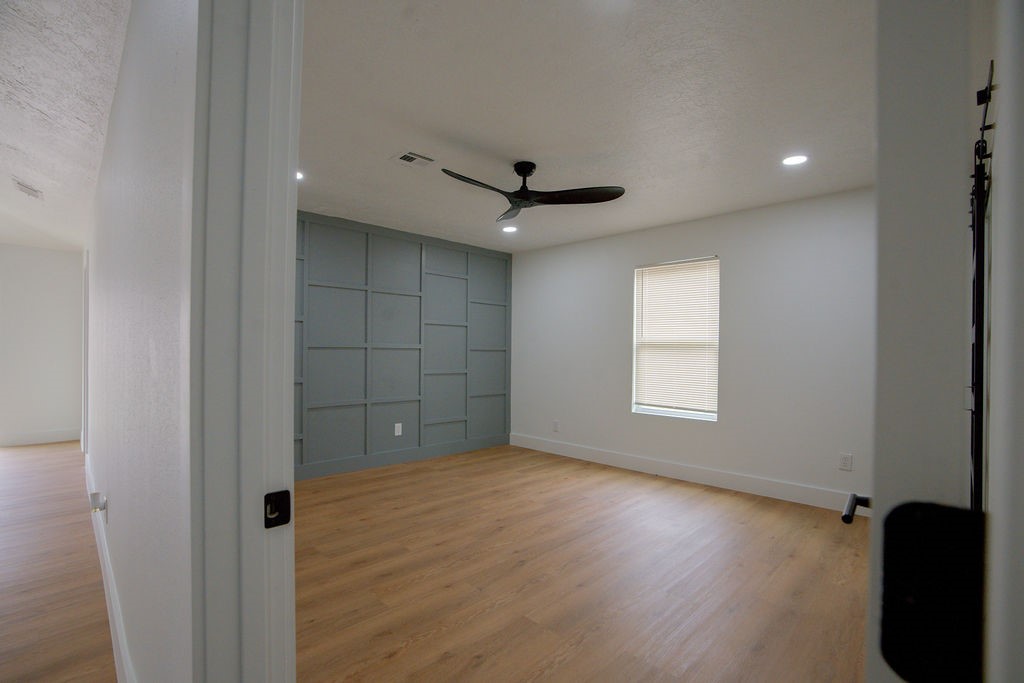 Spacious room with vinyl floors, a stylish accent wall, ceiling fan, and natural light from the window.