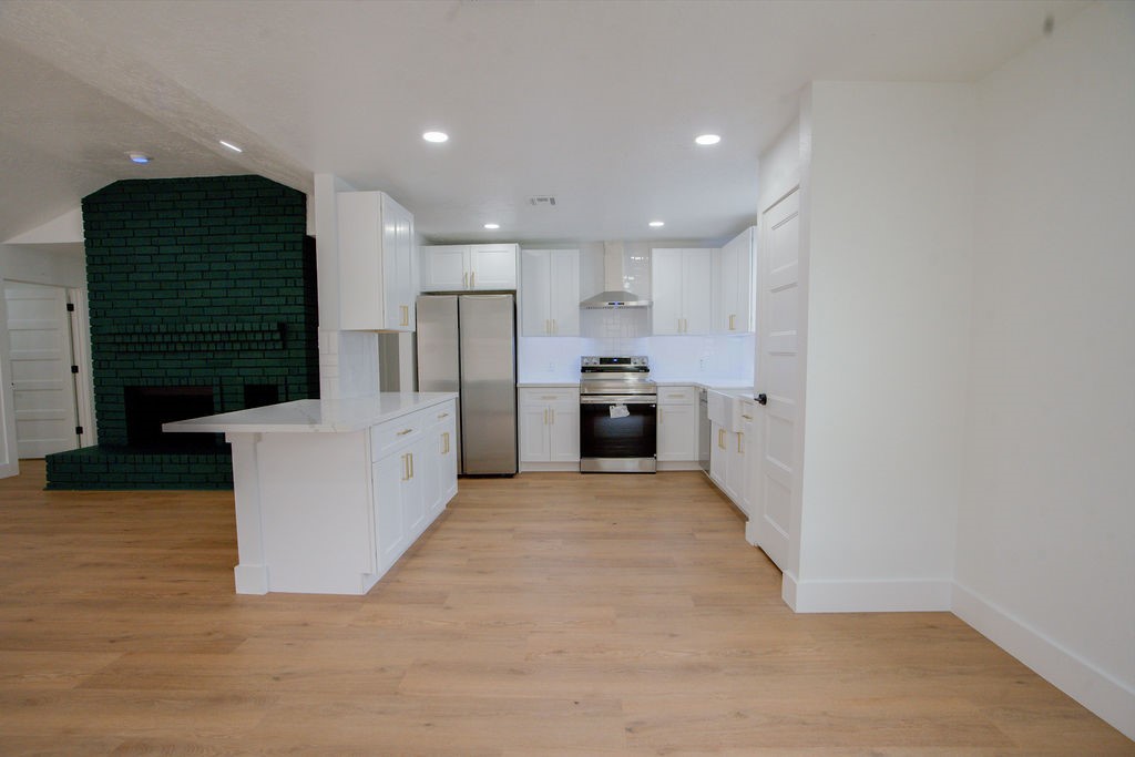 Bright and modern kitchen with sleek white cabinetry, stainless steel appliances, and a stylish dark fireplace accenting the open-concept layout.
