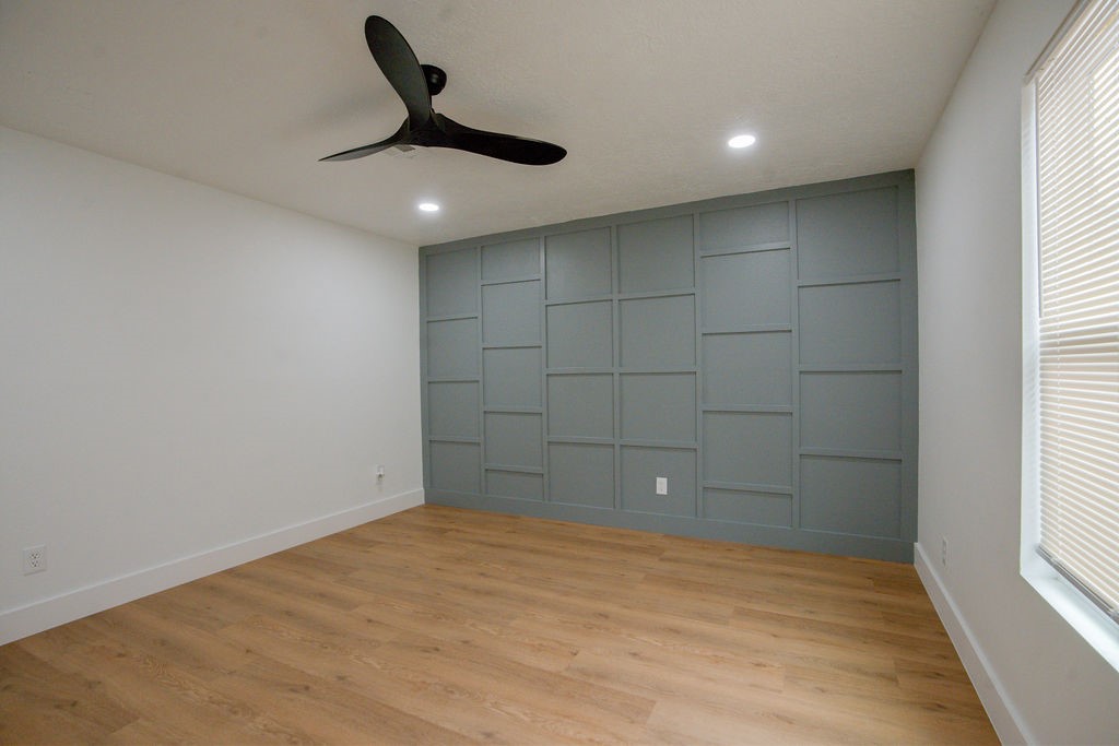 Modern room featuring a stylish accent wall with grid paneling, sleek ceiling fan, and warm wood style flooring, offering a cozy yet contemporary ambiance.