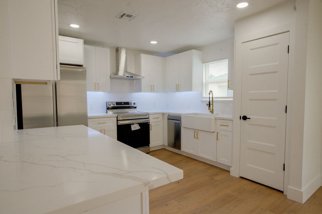 Sleek and modern kitchen featuring white cabinetry, stainless steel appliances, a farmhouse sink, and elegant quartz countertops.
