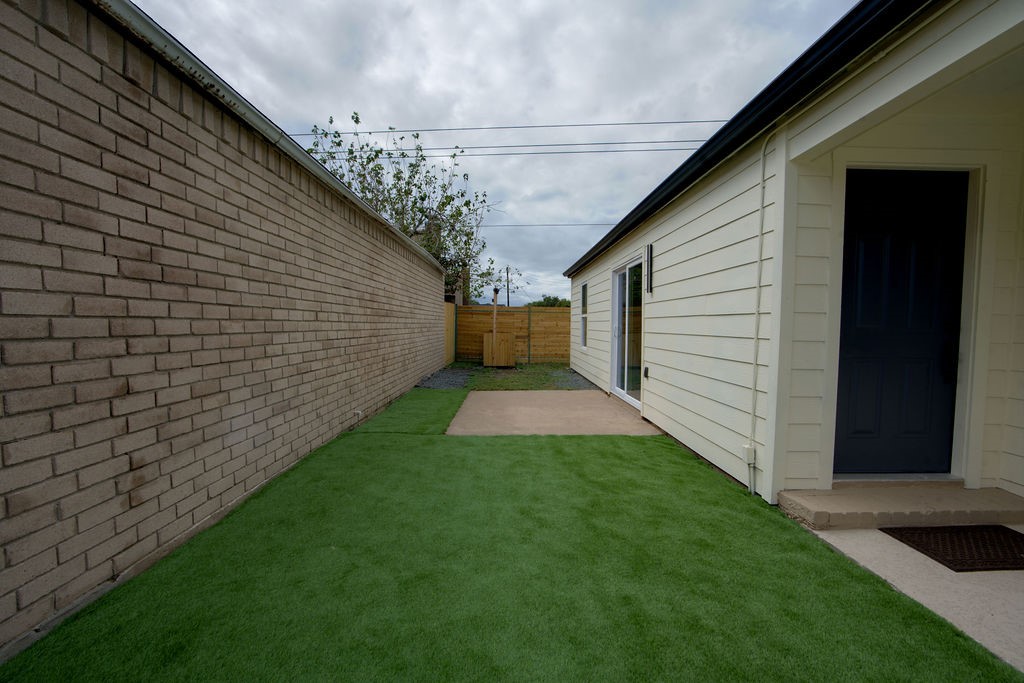 Charming outdoor space featuring a cozy fenced yard with lush green turf and a welcoming entryway, perfect for relaxing or entertaining.