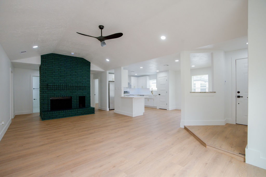 Discover a spacious open-plan living area featuring a striking dark green brick fireplace, modern ceiling fan, and seamless flow into a bright, updated kitchen with sleek finishes.