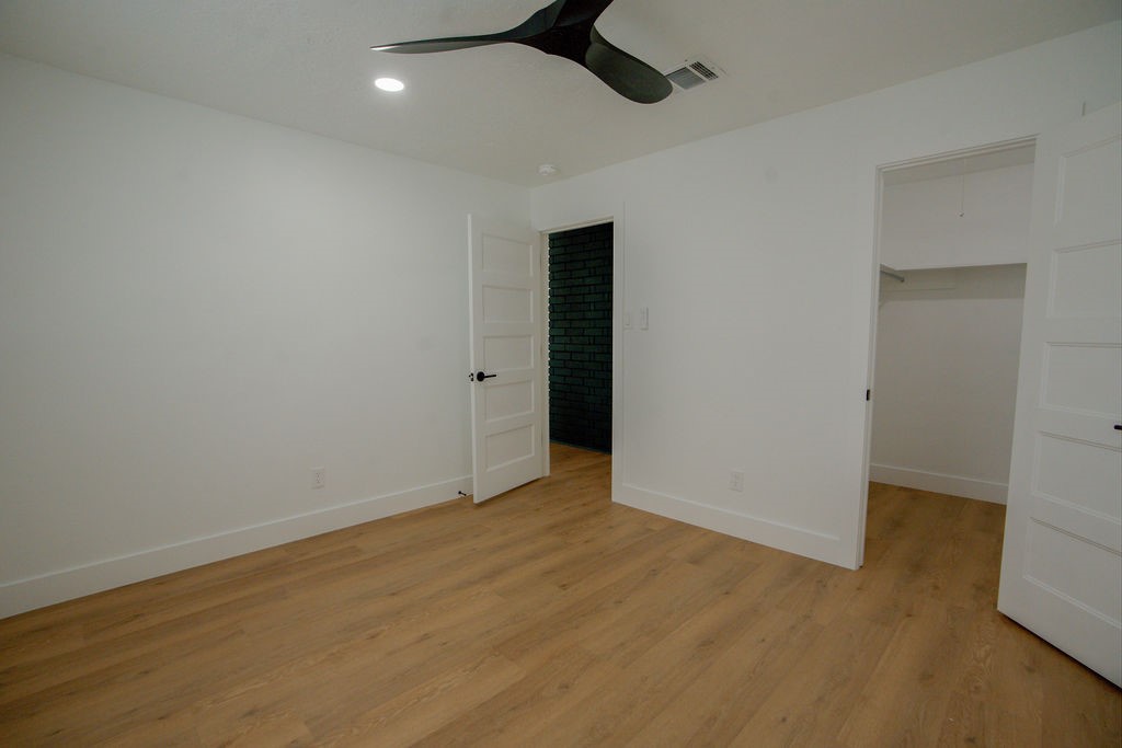 Spacious room with sleek wood style flooring, modern ceiling fan, and ample natural light, featuring a walk-in closet and stylish white doors.
