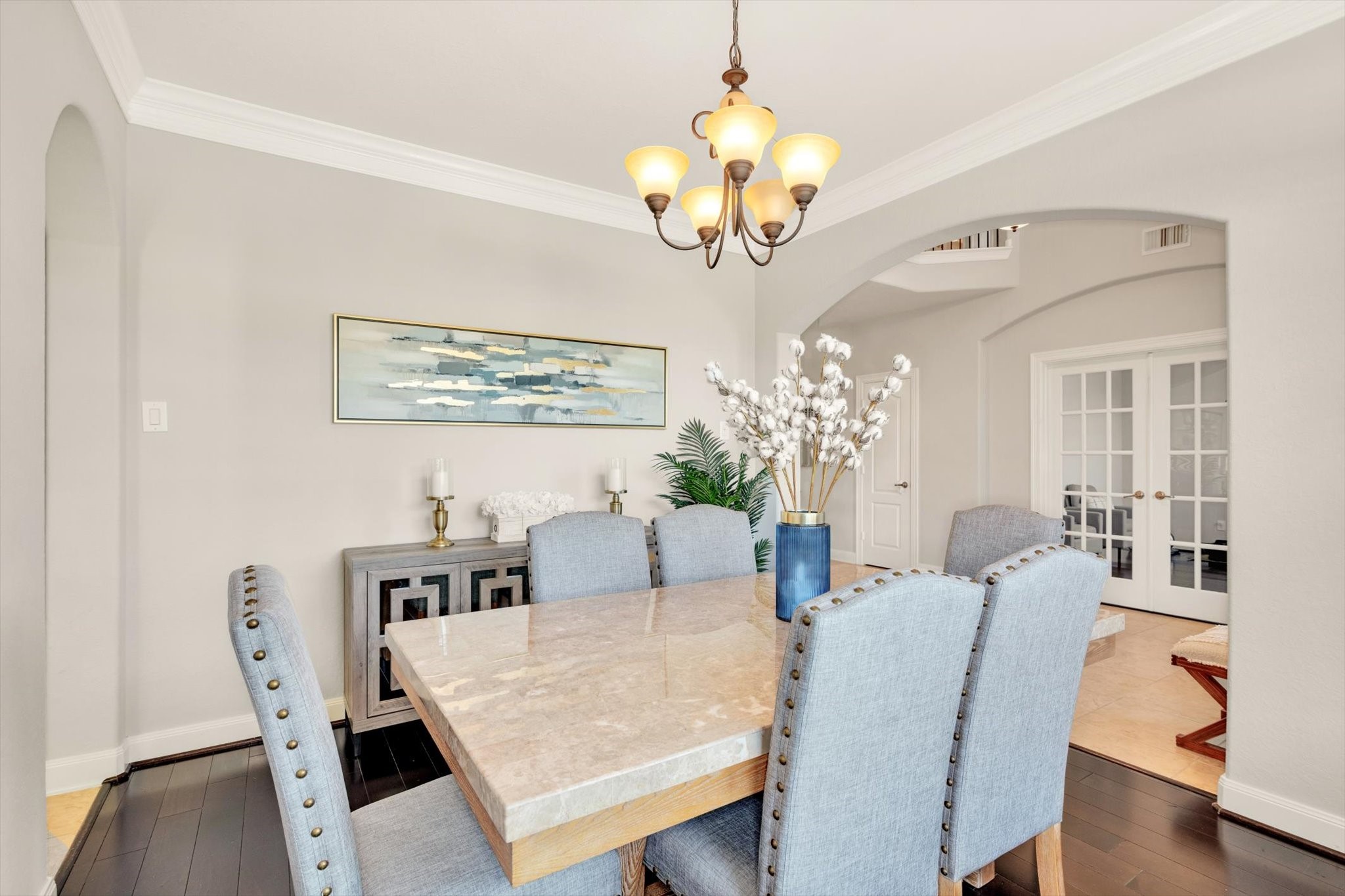 The dining room features elegant decor with a marble-top table and upholstered chairs. It has an inviting ambiance with soft lighting, a modern chandelier, and is accented by tasteful artwork and a sideboard.