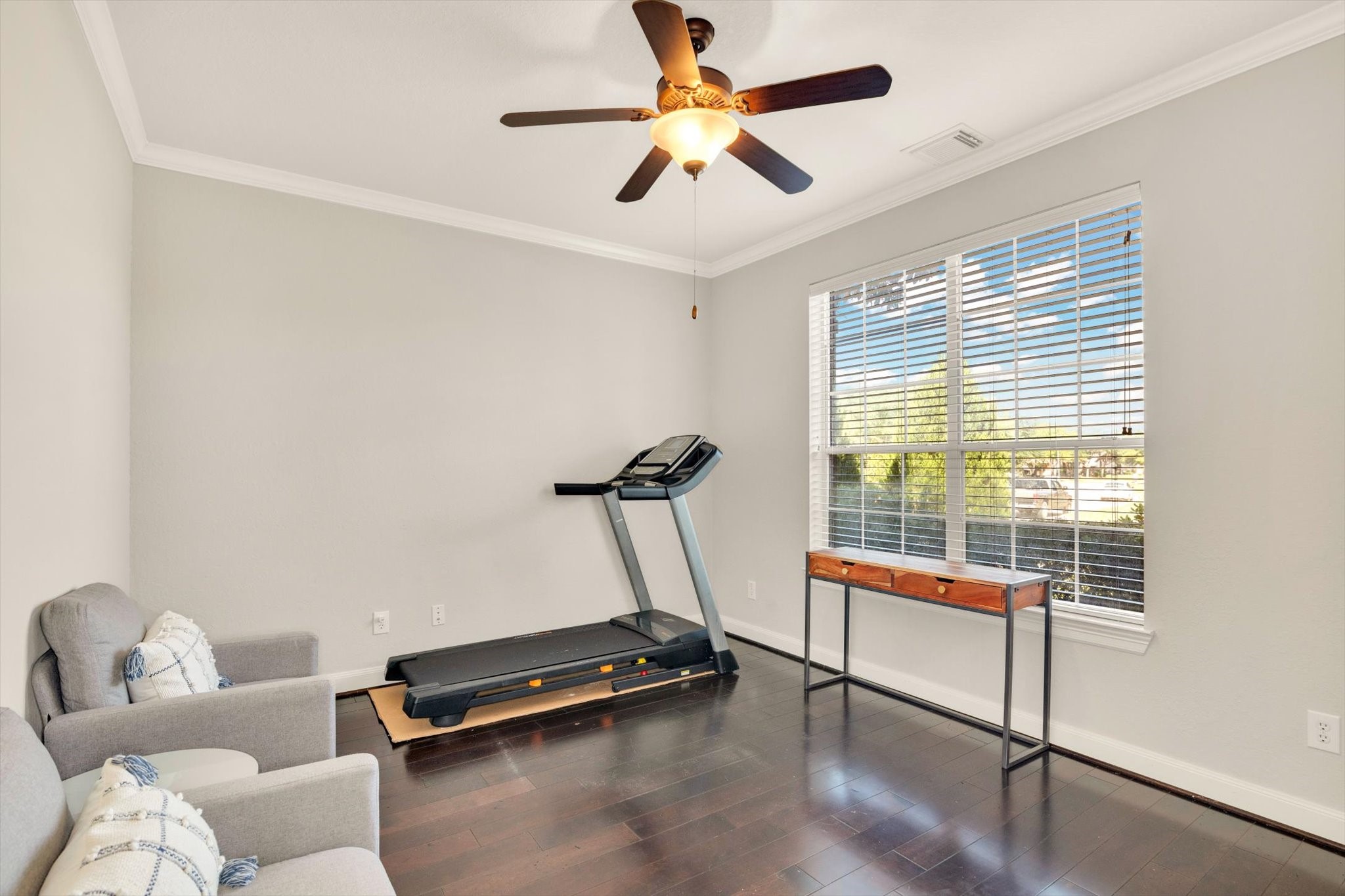 Home Office or Flex room with hardwood flooring, featuring a large window for natural light, a ceiling fan, and space for a treadmill and seating.