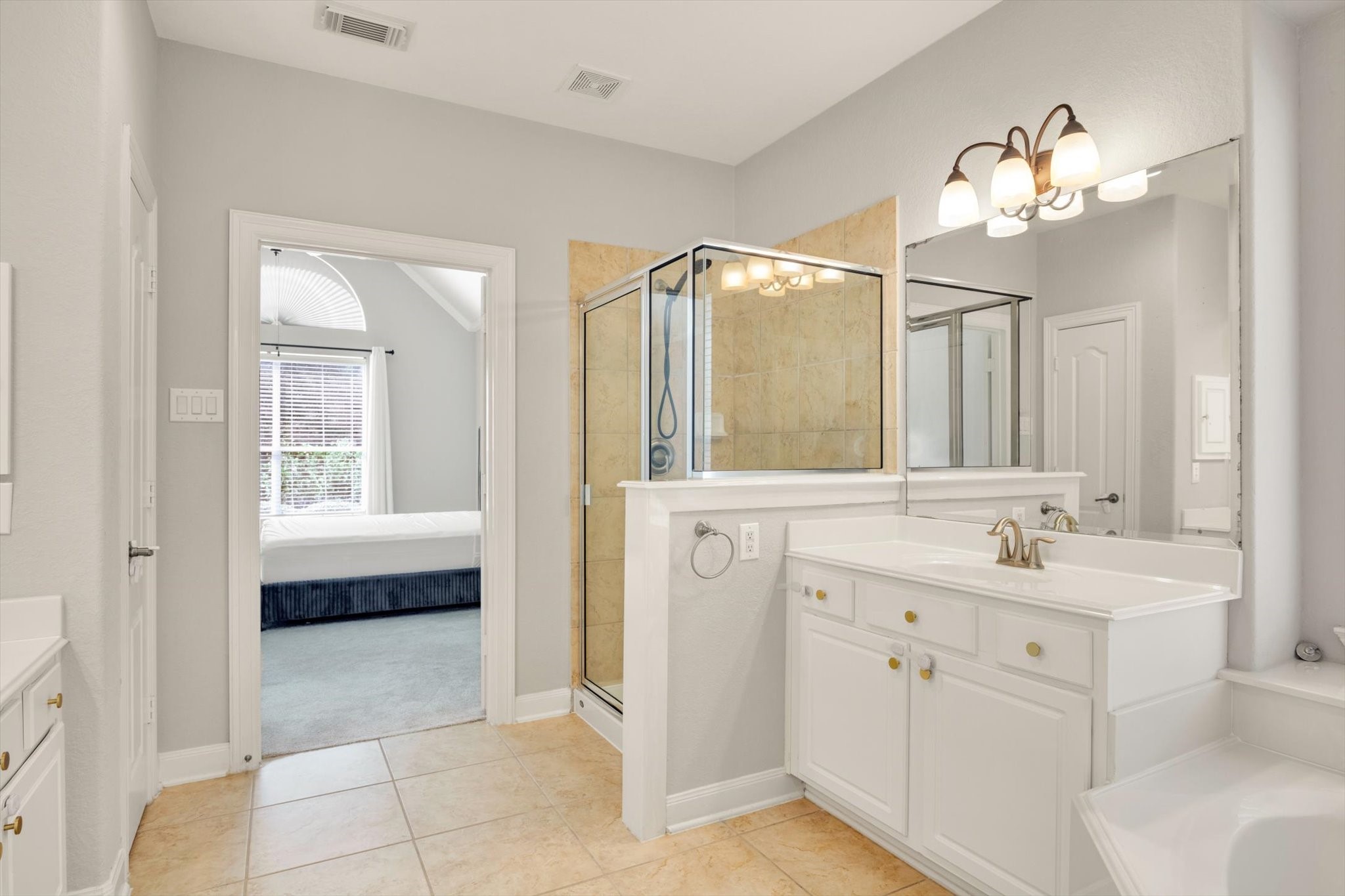 Bright and spacious bathroom featuring a glass-enclosed shower, dual sinks with elegant fixtures, and ample cabinet storage.
