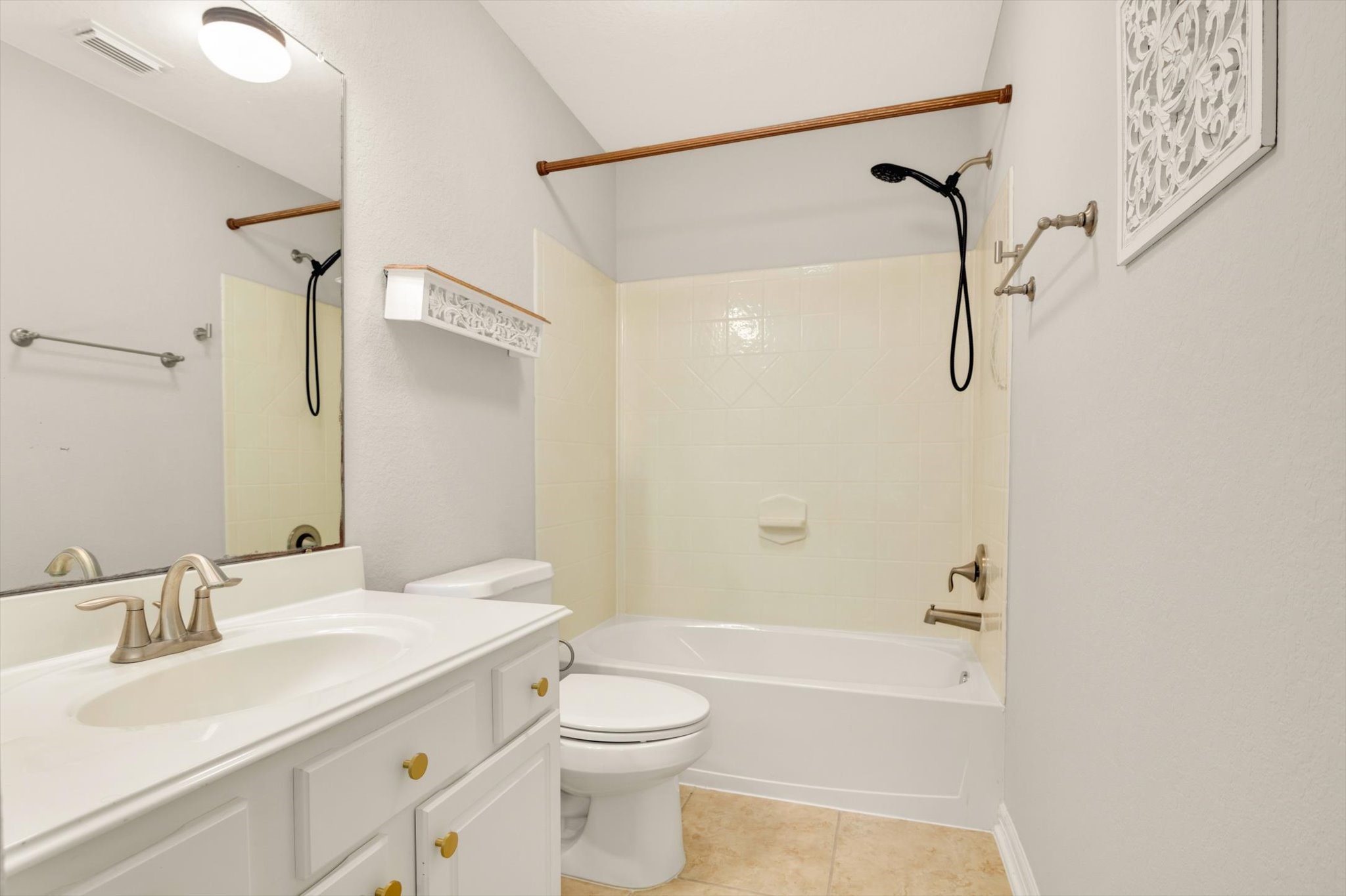 Secondary bathroom features a clean, modern design with light walls and tile flooring. It includes a bathtub with a shower, a white vanity with storage, and a large mirror, creating a bright and functional space.