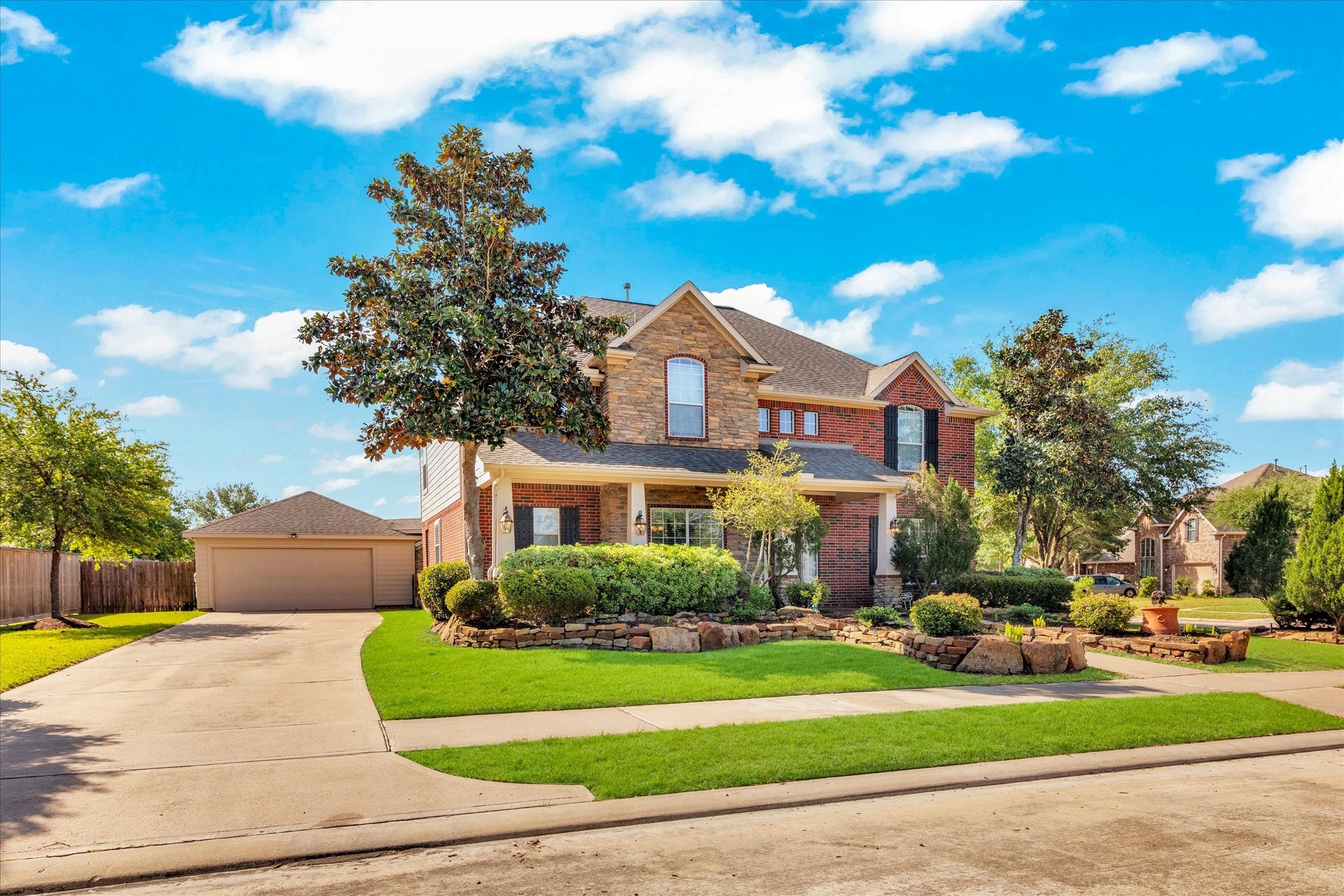 Formel model home with a well-manicured lawn and mature trees. The property features a spacious driveway leading to a detached garage, and attractive landscaping enhances its curb appeal.