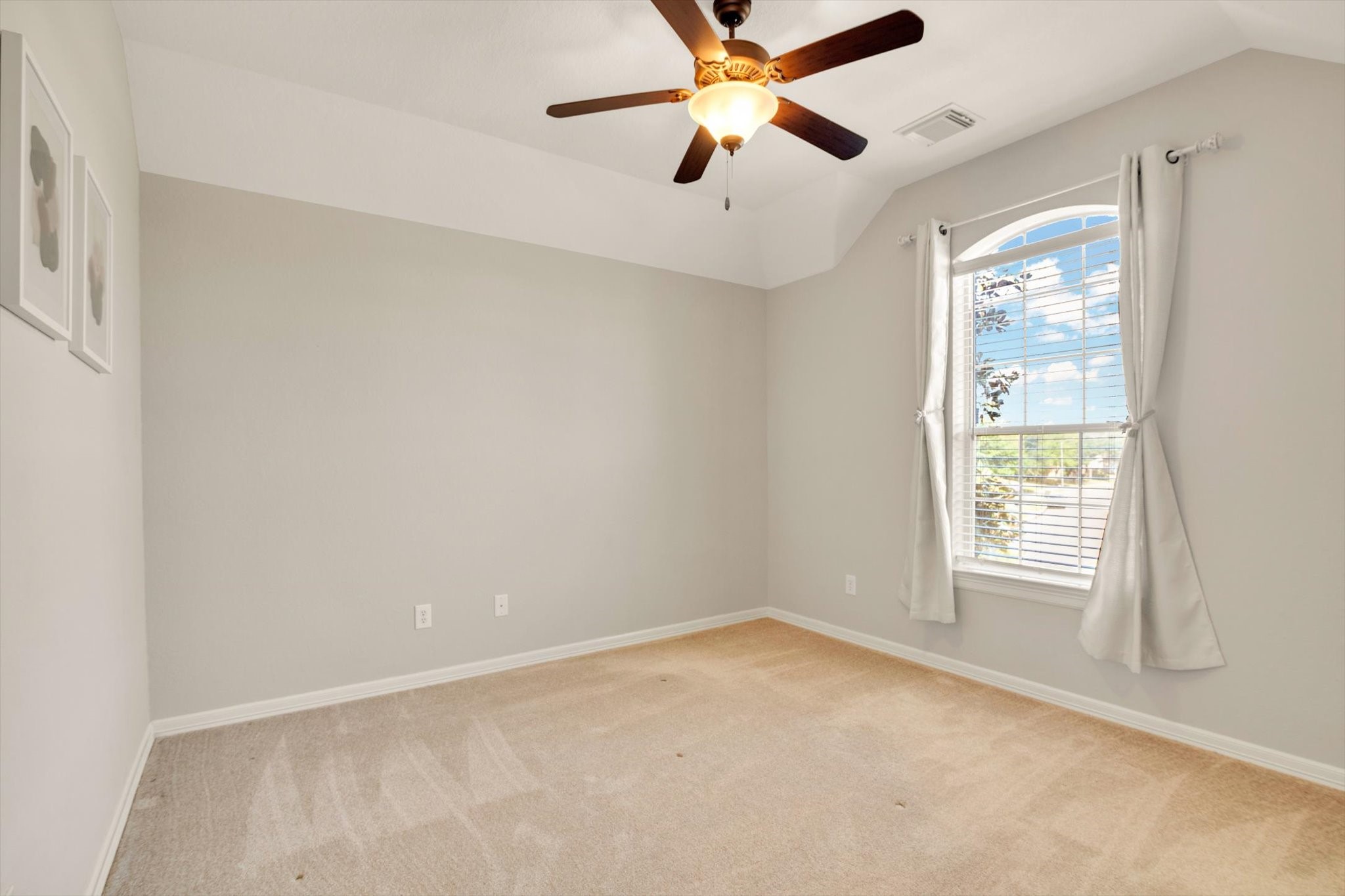 Secondary Bedroom features neutral walls and carpet, a ceiling fan with light, and a large window with drapes, providing plenty of natural light. Perfect for a bedroom or office space.