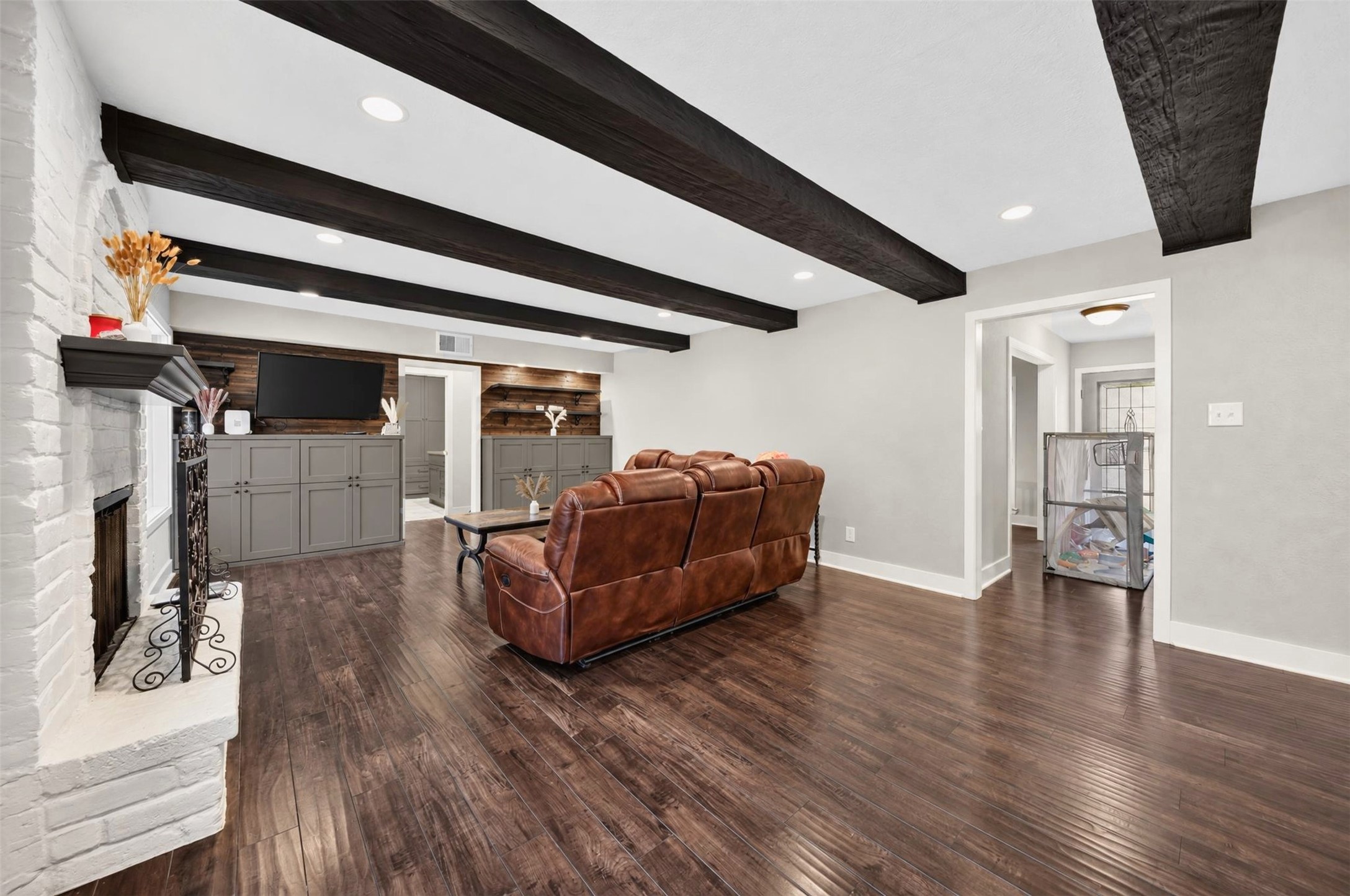 Spacious Living Room
Expansive living room showcasing beautiful wood flooring, dramatic exposed ceiling beams, a painted brick fireplace, recessed lighting, and custom built-in cabinetry with wood accent details.