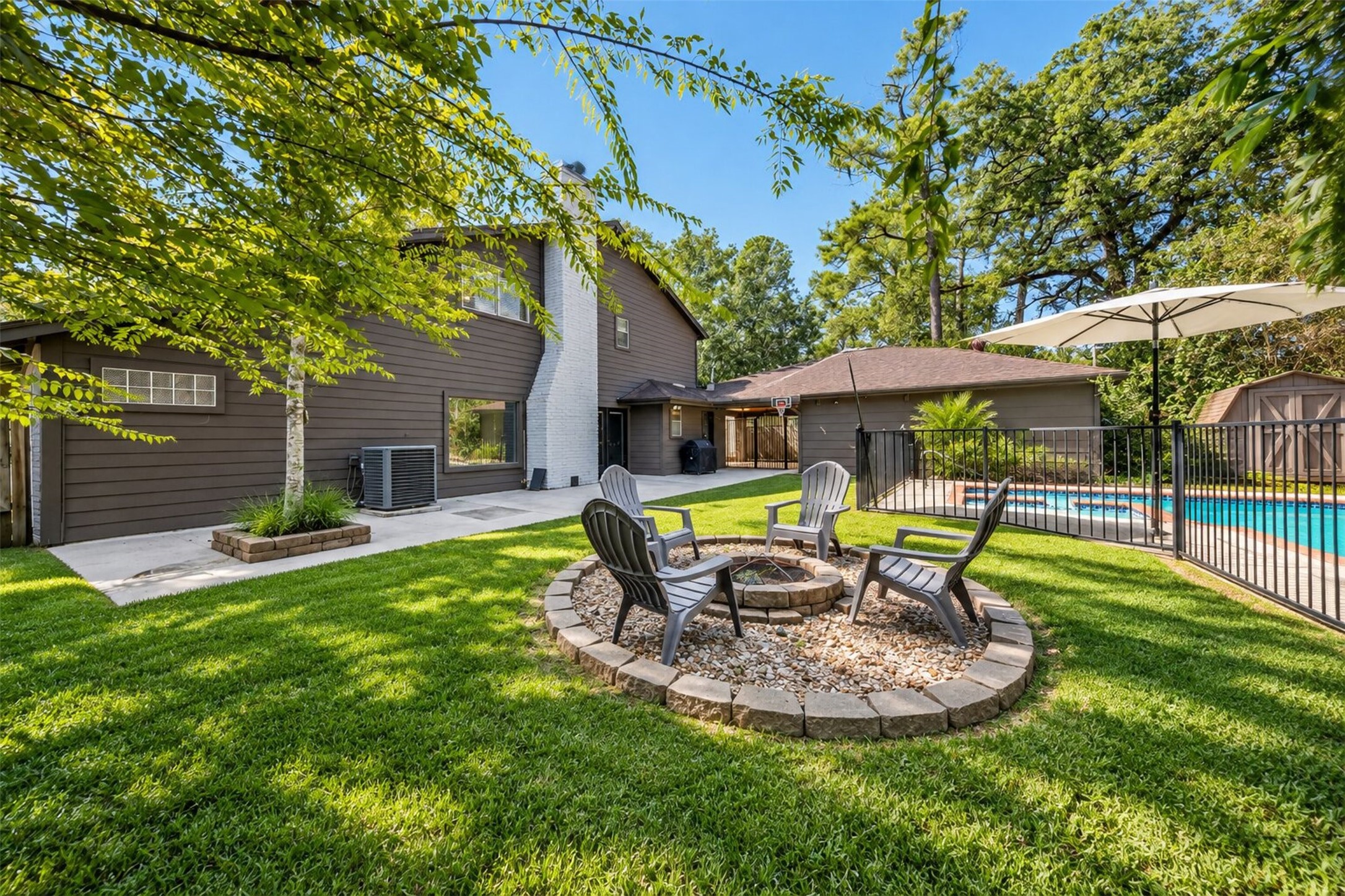Backyard Retreat: Expansive backyard featuring lush green lawn, mature shade trees, a dedicated fire pit seating area, and a private fenced pool.