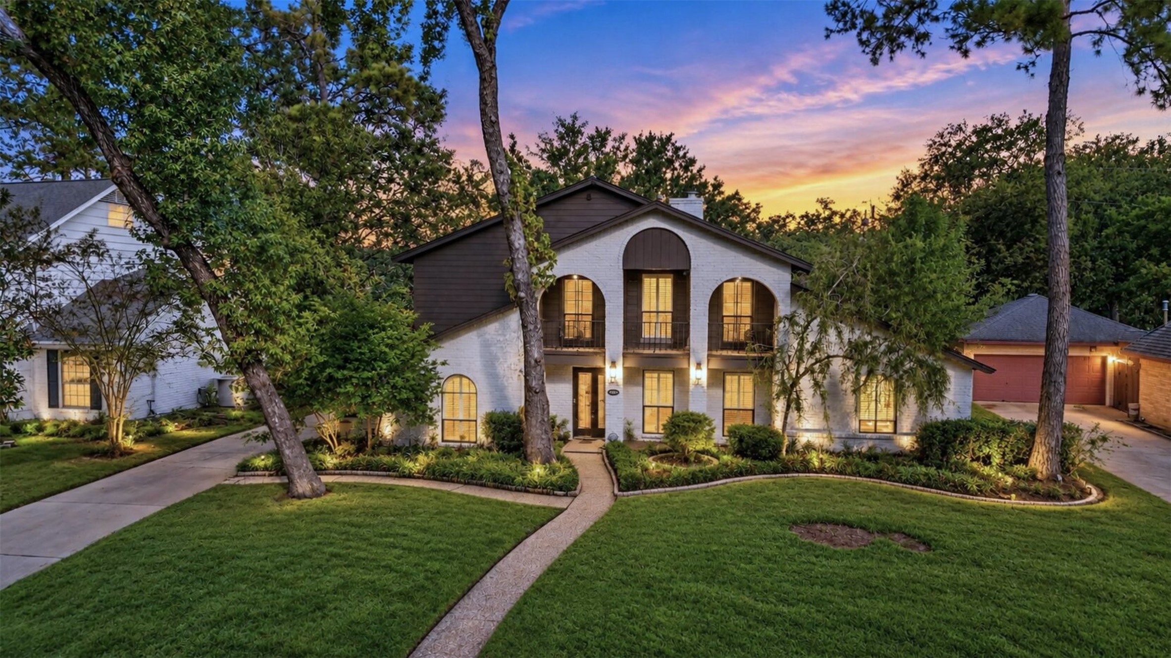Twilight Front Exterior: Stunning twilight view showcasing the home's distinctive architecture, arched windows, second-story balcony, and beautifully landscaped front yard.