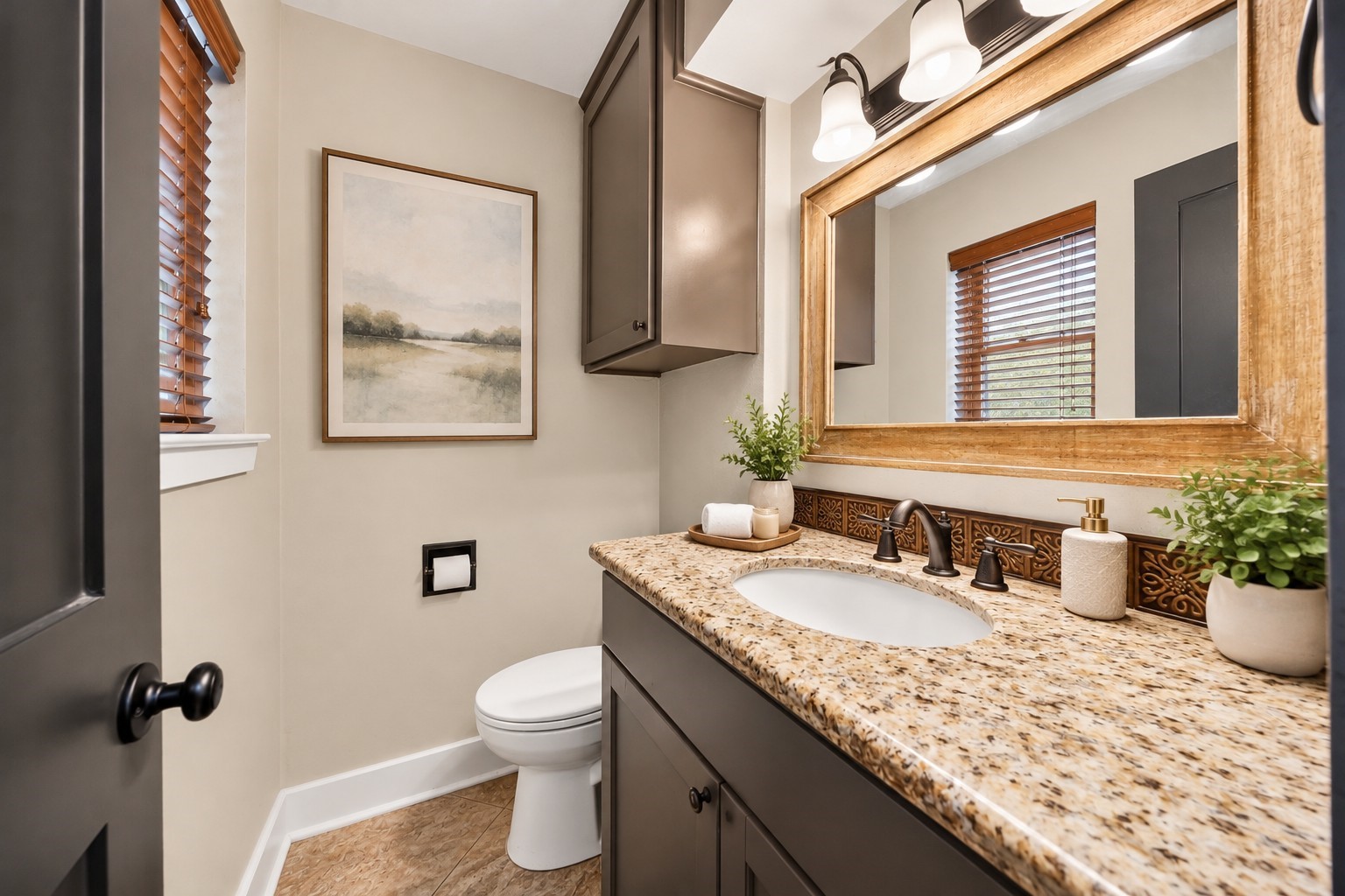 Half Bathroom (Virtually Staged)
Charming powder bathroom featuring a granite countertop, gray vanity cabinetry, decorative tile backsplash, wood-framed mirror, and natural light from the window.