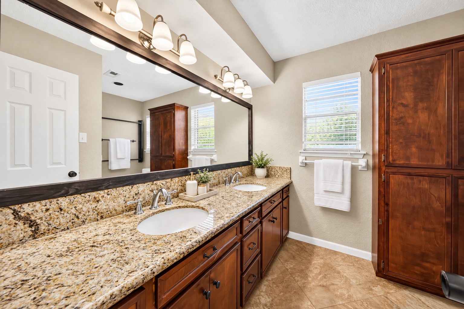 Secondary Bathroom
Spacious primary bathroom featuring an expansive double-sink vanity, granite countertops, rich wood cabinetry, oversized framed mirror, and abundant storage. Natural light creates a bright, welcoming atmosphere.
