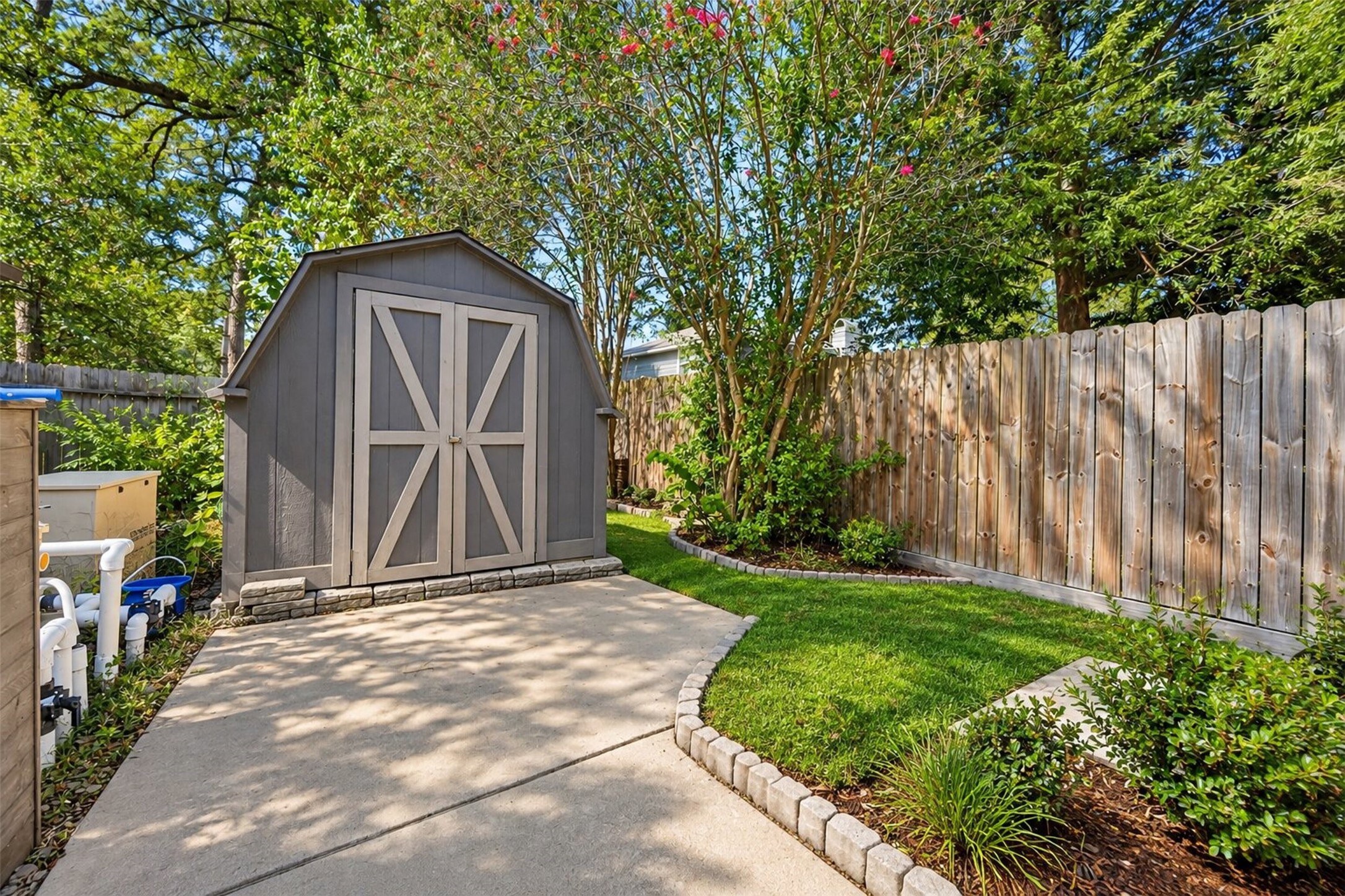 Backyard Storage: Convenient outdoor storage shed surrounded by mature landscaping, a privacy fence, and a paved walkway for easy access.