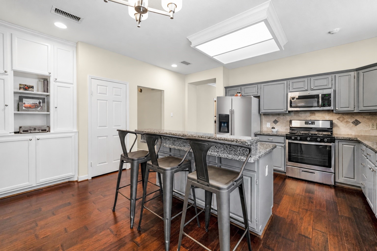 Charming kitchen with modern gray cabinetry, stainless steel appliances, and a spacious granite-topped island that offers casual seating. Warm wood flooring enhances the inviting atmosphere, complemented by built-in shelving for additional storage. Charming kitchen with modern gray cabinetry, stainless steel appliances, and a spacious granite-topped island that offers casual seating. Warm wood flooring enhances the inviting atmosphere, complemented by built-in shelving for additional storage.