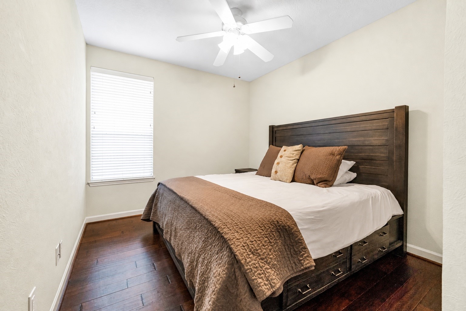 Cozy second bedroom featuring a stylish wooden bed frame, warm bedding, and a bright window, all complemented by elegant hardwood floors.