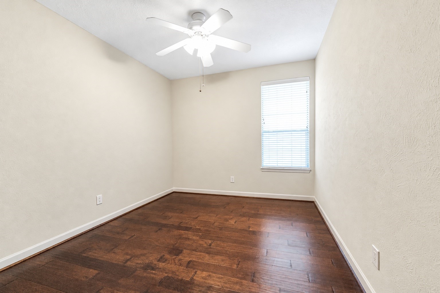 Bright and cozy dining with warm hardwood floors, a ceiling fan, and ample natural light from a large window.
